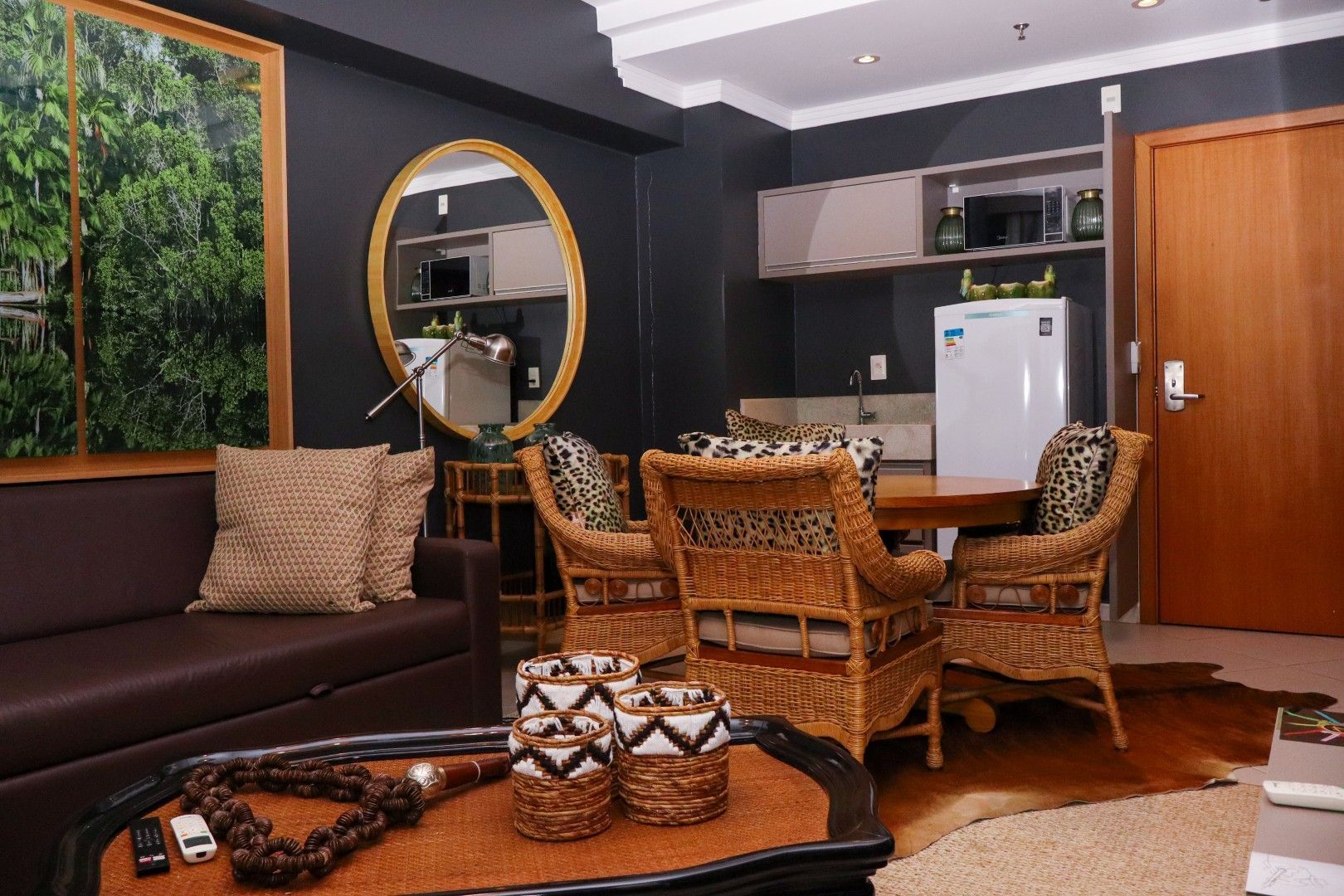 Sala de estar com paredes cinza-escuras, um sofá, área de jantar e um grande espelho redondo.