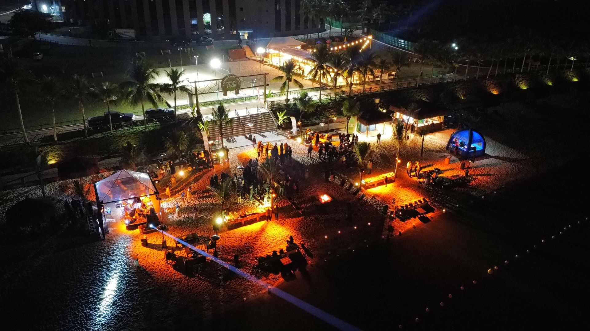 Conferência com apresentadores no palco e público sentado. Iluminação azul e vermelha.