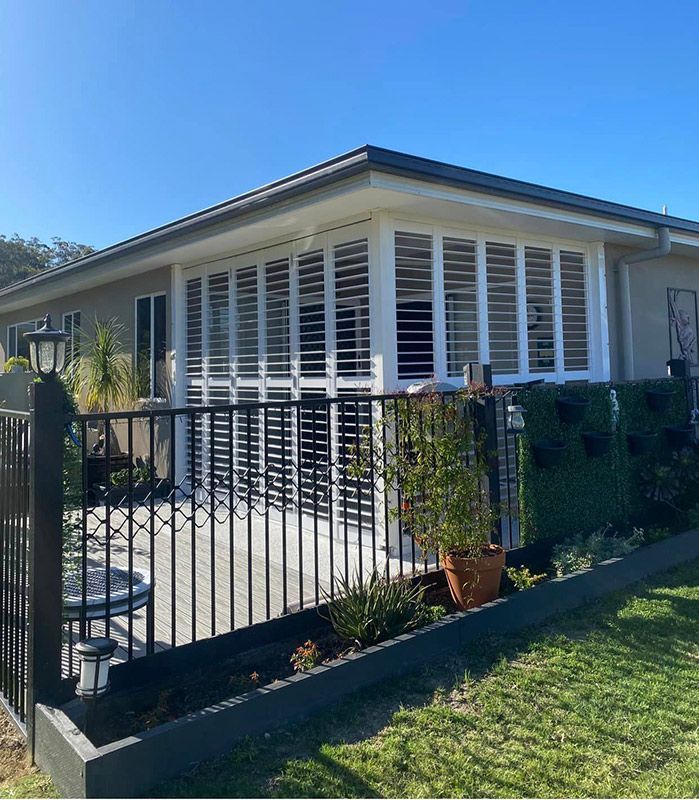 A House With White Shutters On The Windows And A Black Fence — Window Coverings in Gold Coast, QLD