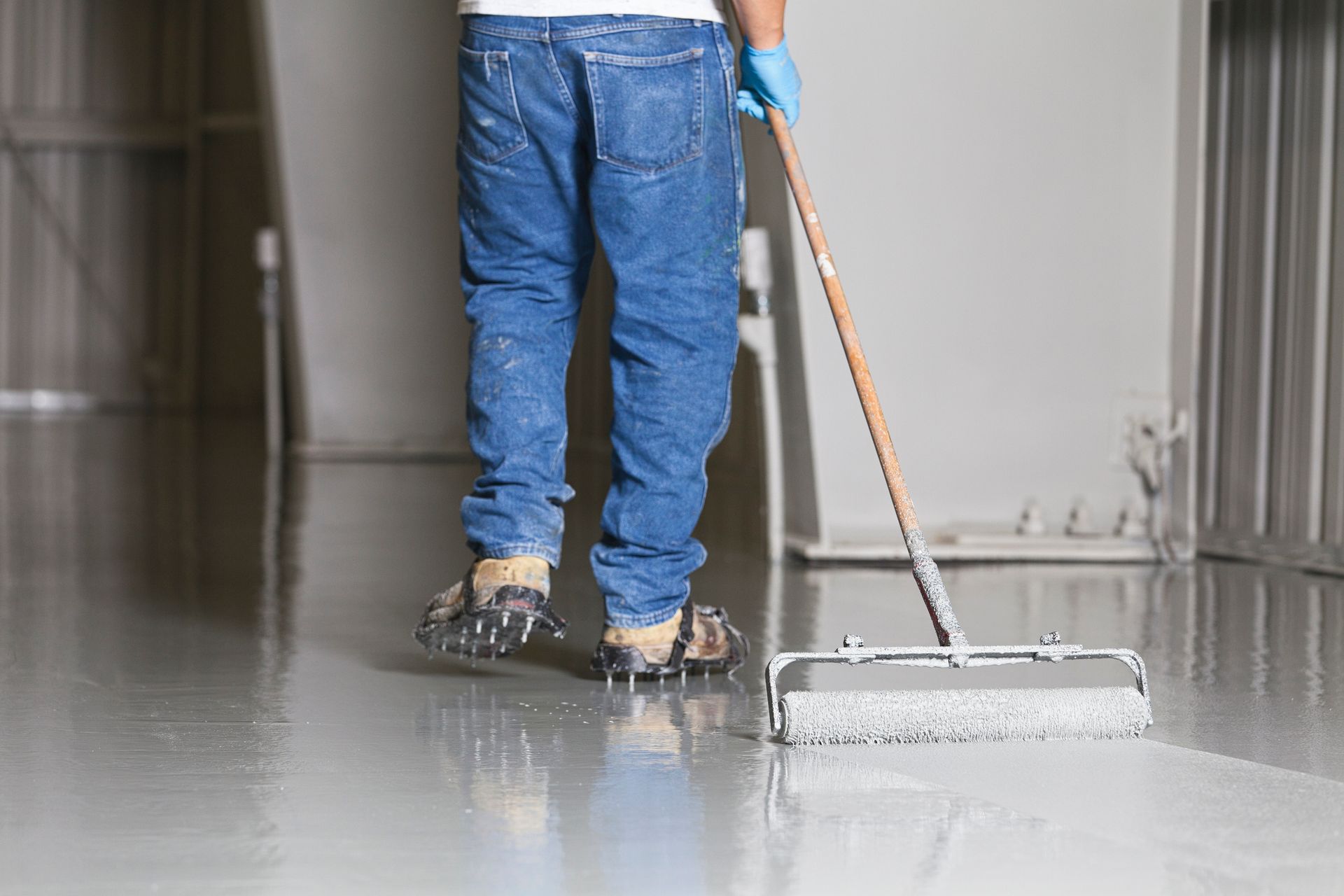 A man is painting a concrete floor with a roller. - Dura Garage Floors - Overland Park, Kansas