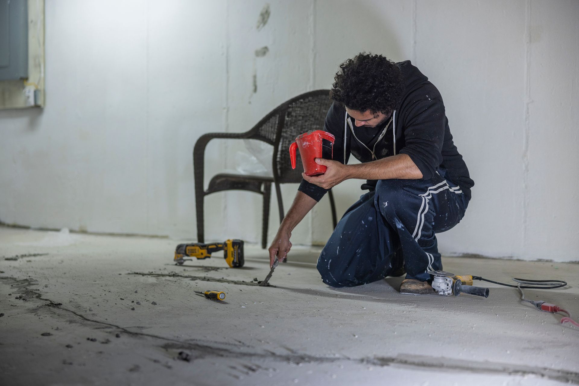A man is kneeling down on the floor using a drill. - Dura Garage Floors - Overland Park, Kansas