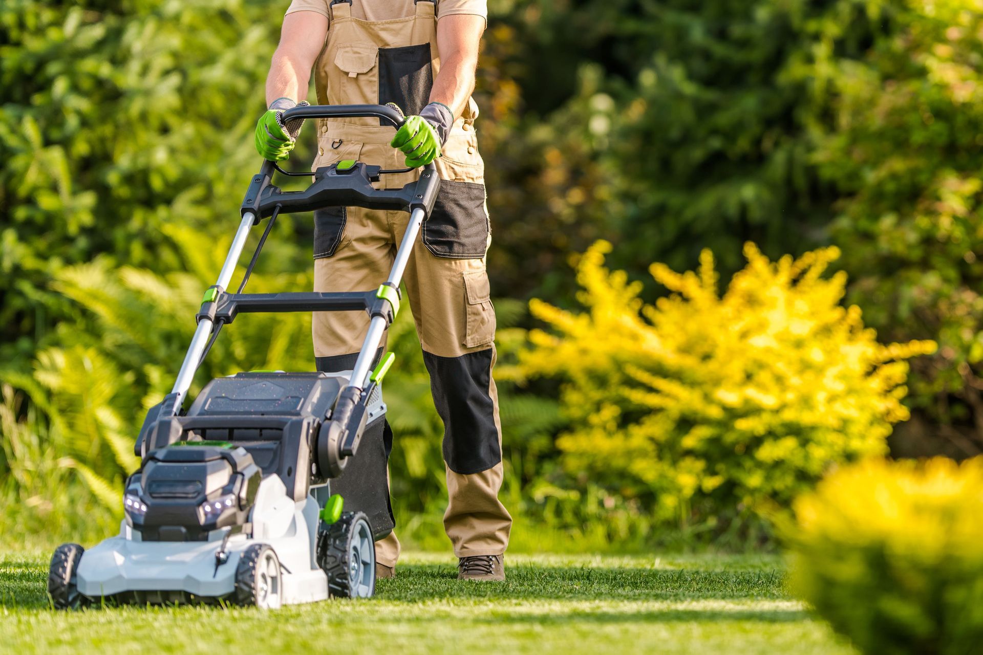 A man is pushing a lawn mower on a lush green lawn.