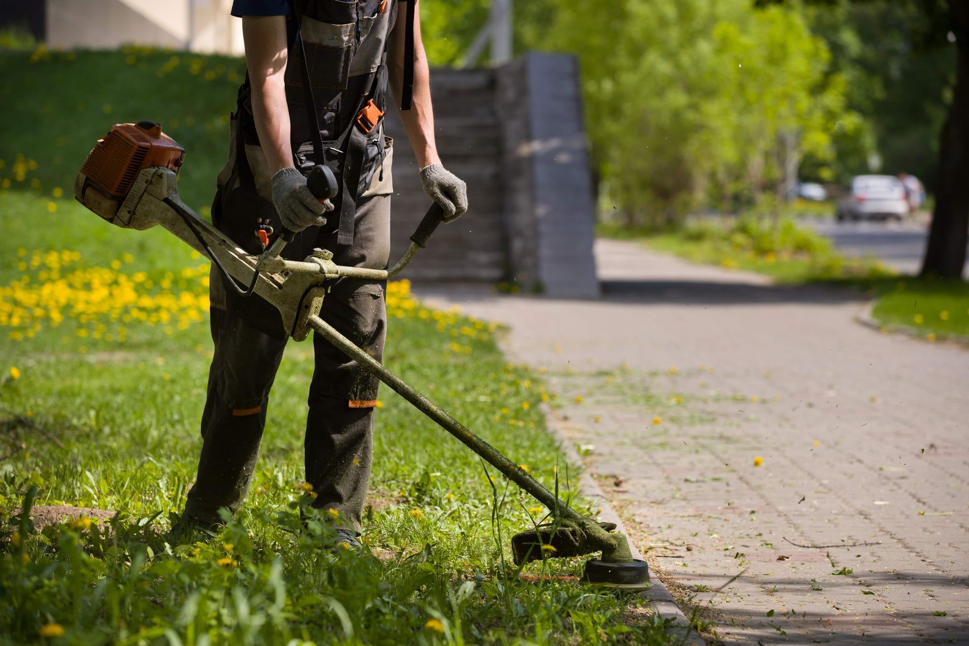 A man is cutting grass with a lawn mower on a sidewalk.