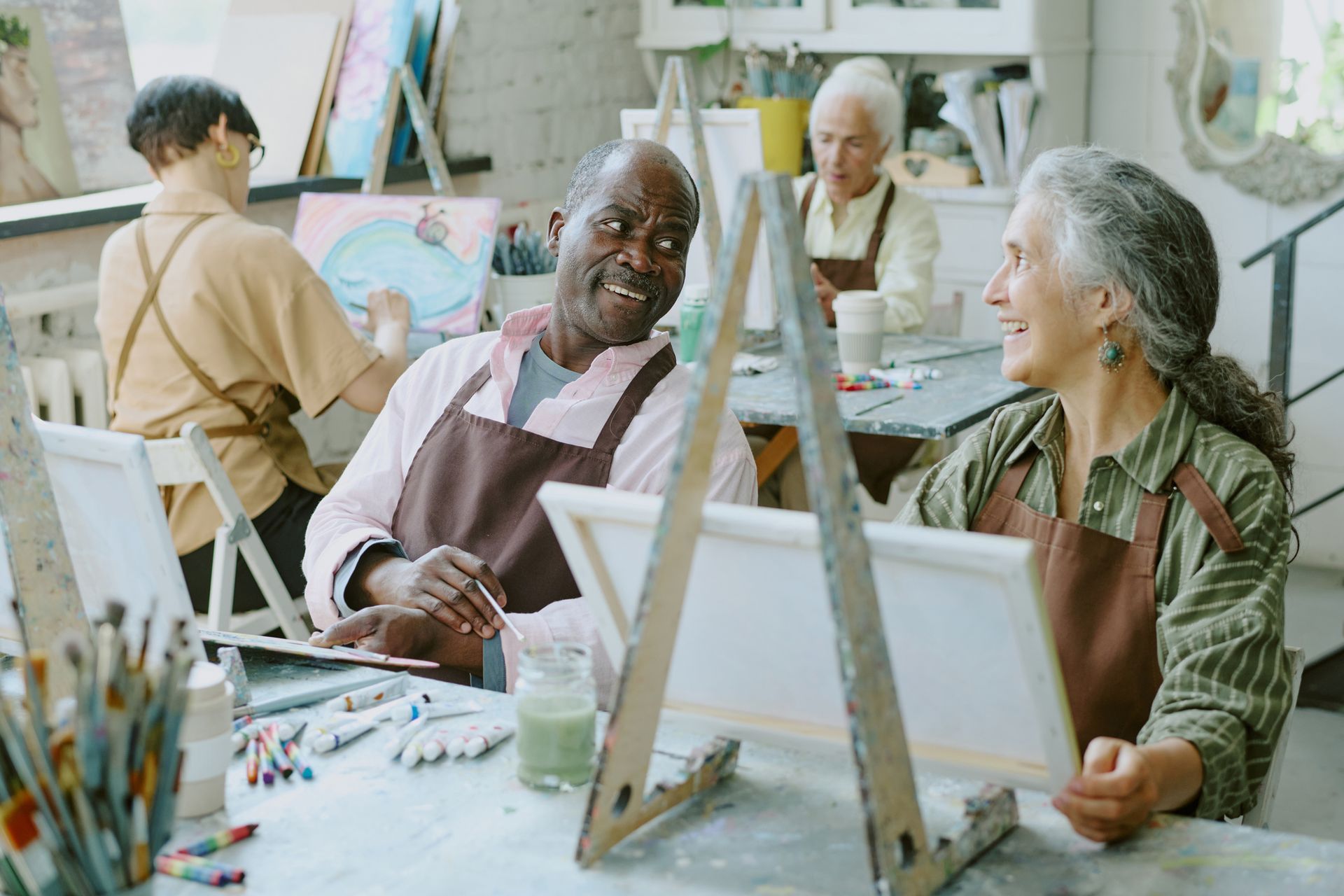People in an art class painting, laughing, with easels and paint supplies.