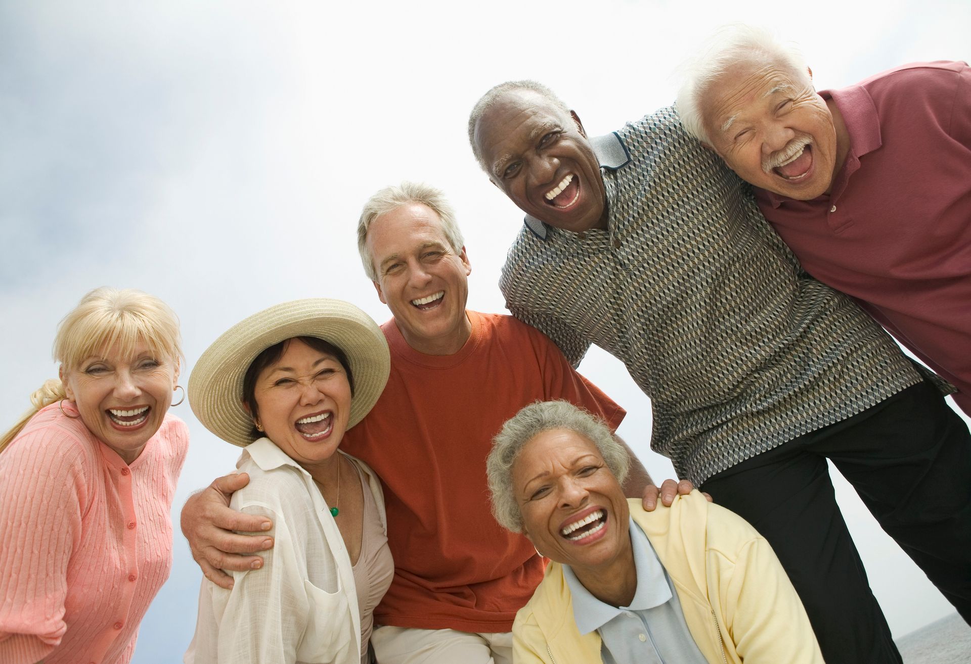 Group of smiling people, diverse in appearance, gathered closely, looking up.