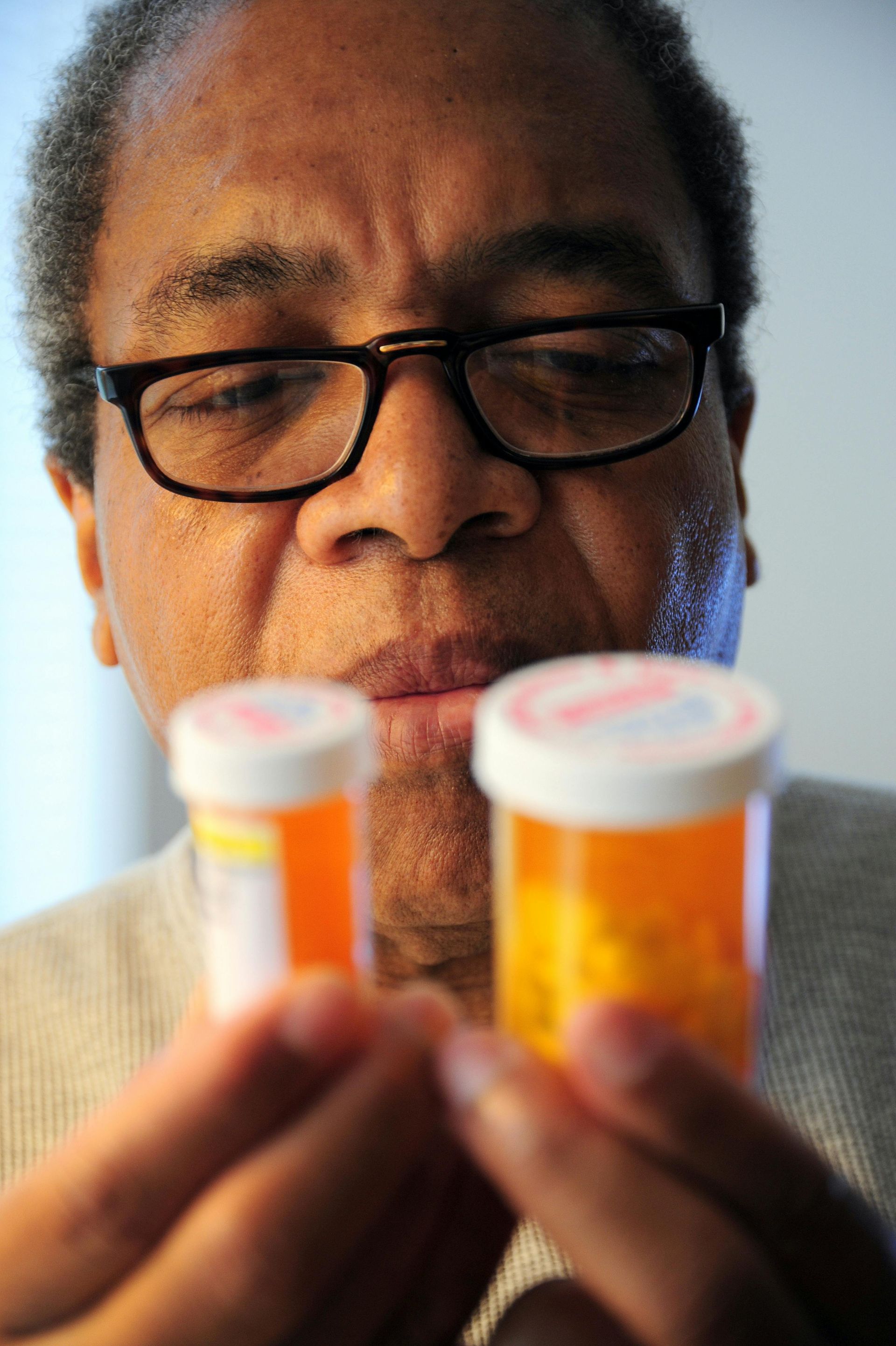 Man with glasses examines two prescription pill bottles.