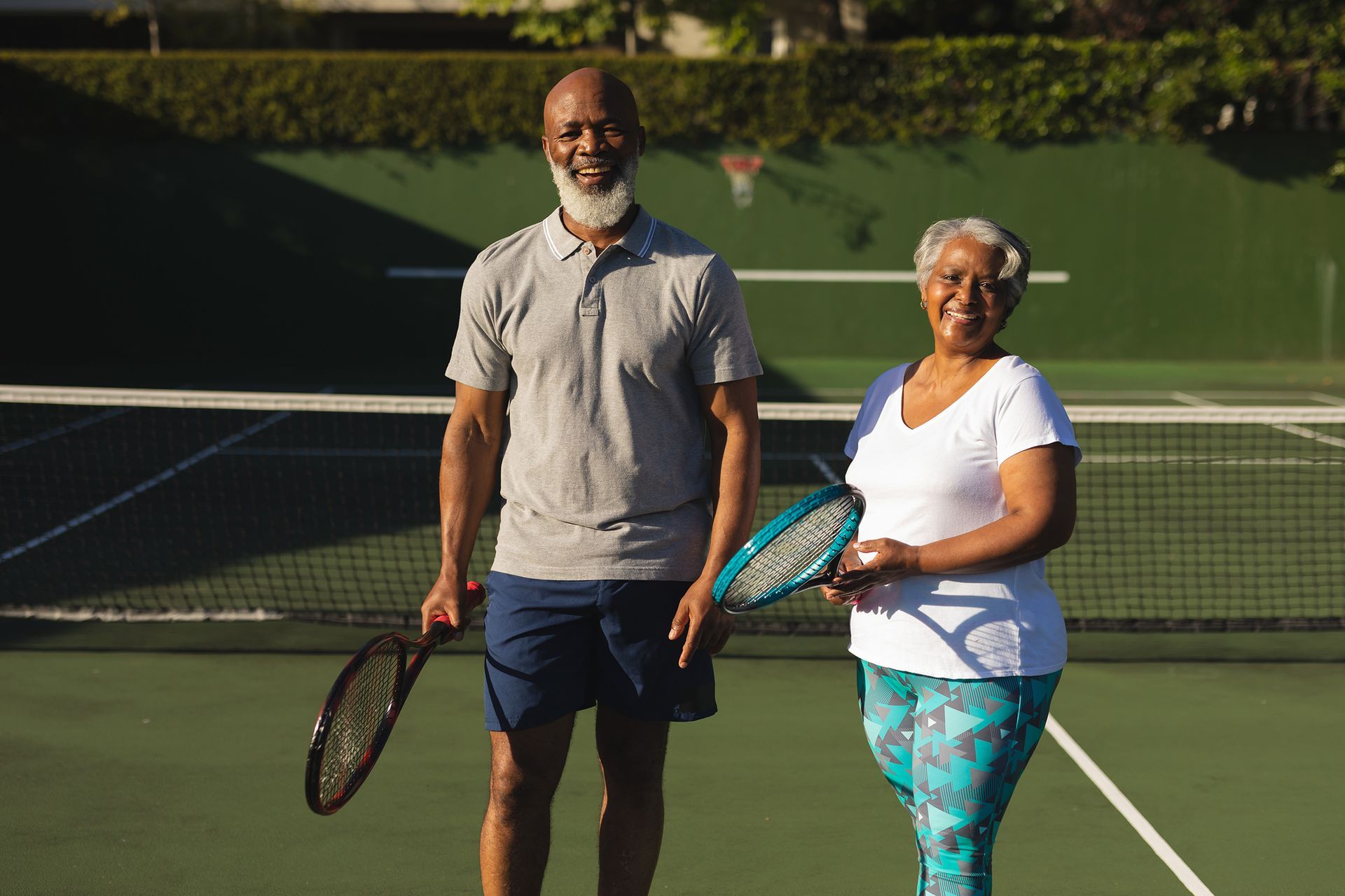 Couple holding tennis rackets on a green court, smiling.