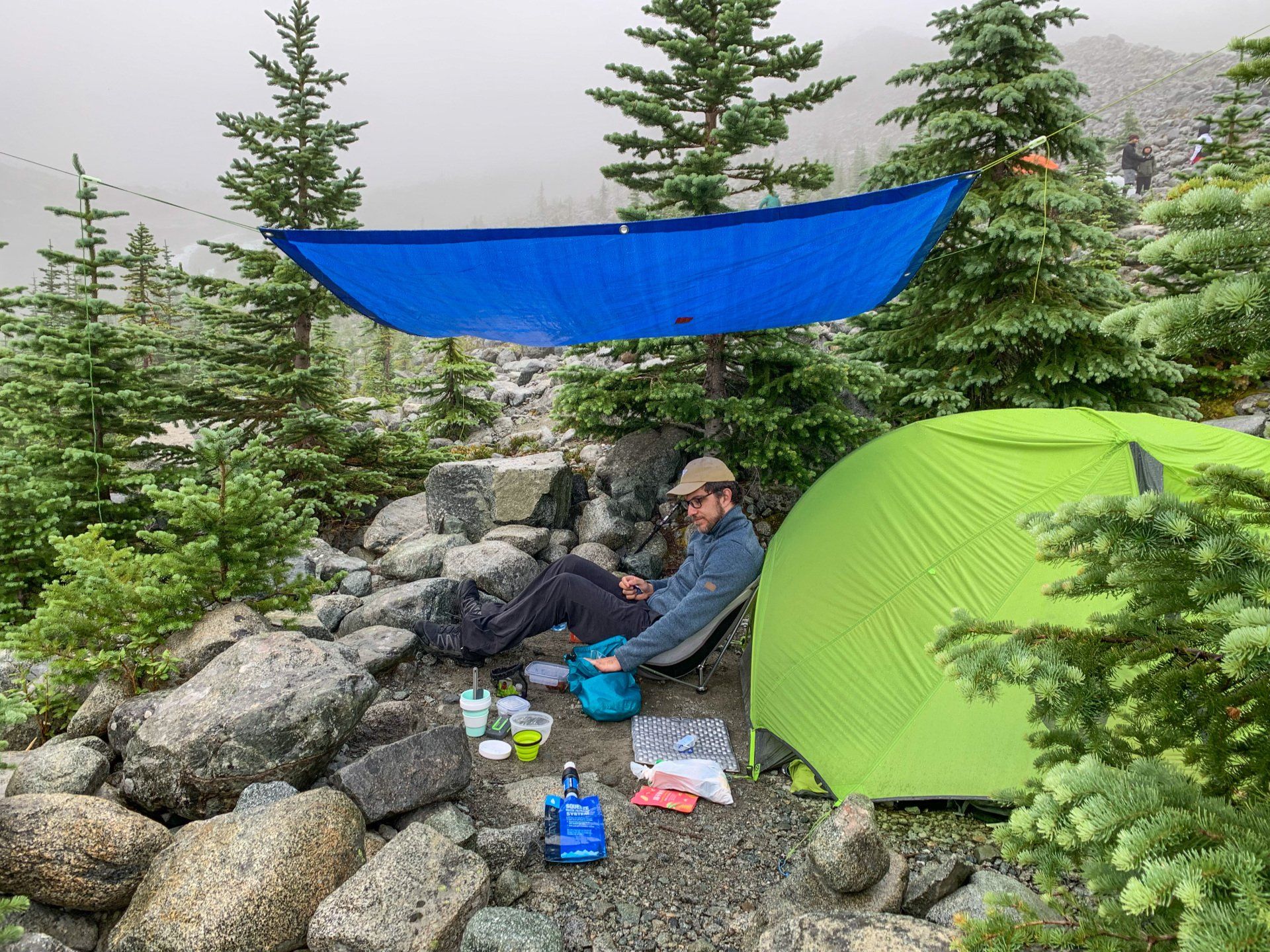 Nemo Dragonfly tent, a tarp hanging near it and a backpacker preparing breakfast. Joffre lakes provincial park, BC, Canada
