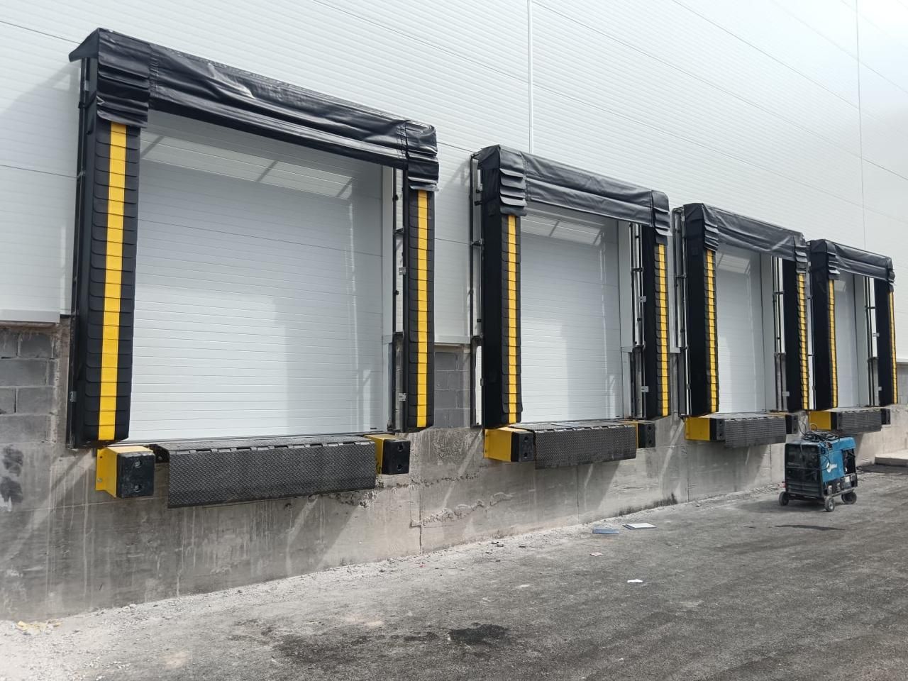 Puertas de muelle de carga en un edificio blanco con juntas negras y detalles amarillos.
