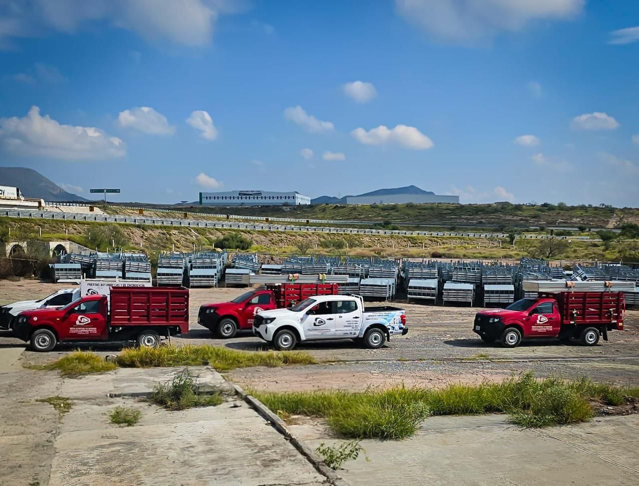 Varios camiones rojos y blancos con logotipos de empresas aparcados en un estacionamiento, con muchos más camiones plateados al fondo.