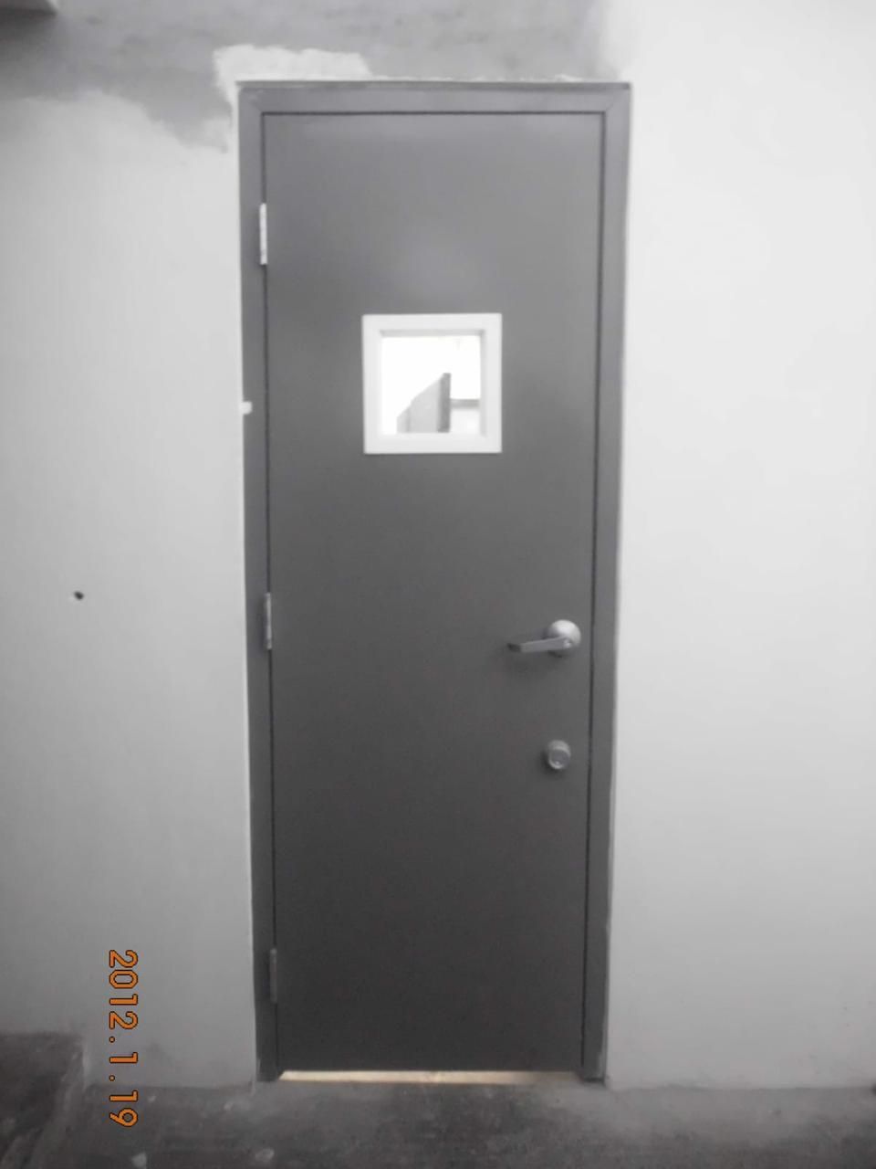 Puerta gris con ventana, enmarcada en una pared blanca.