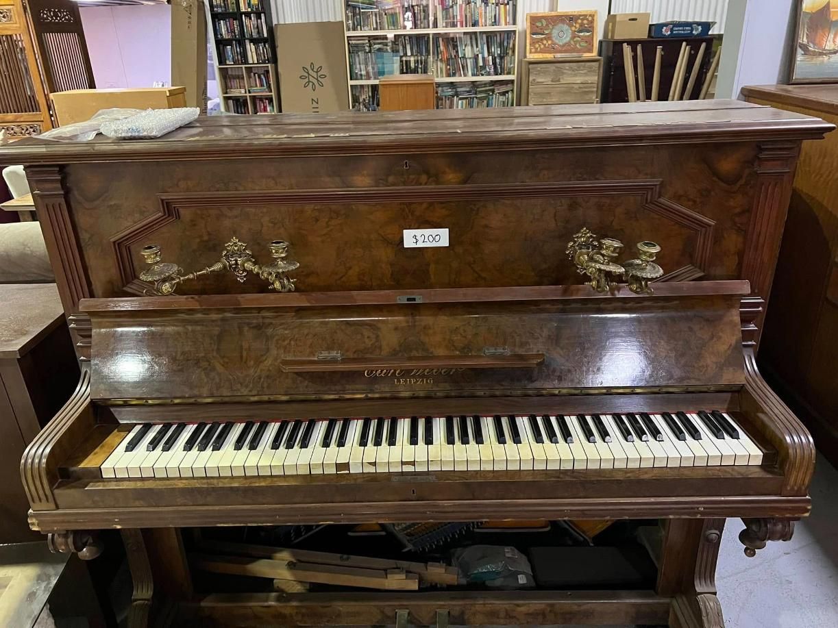 An Old Piano is Sitting in a Room Next to a Bookshelf — Anton's New & Used Furniture In Ciccone, NT