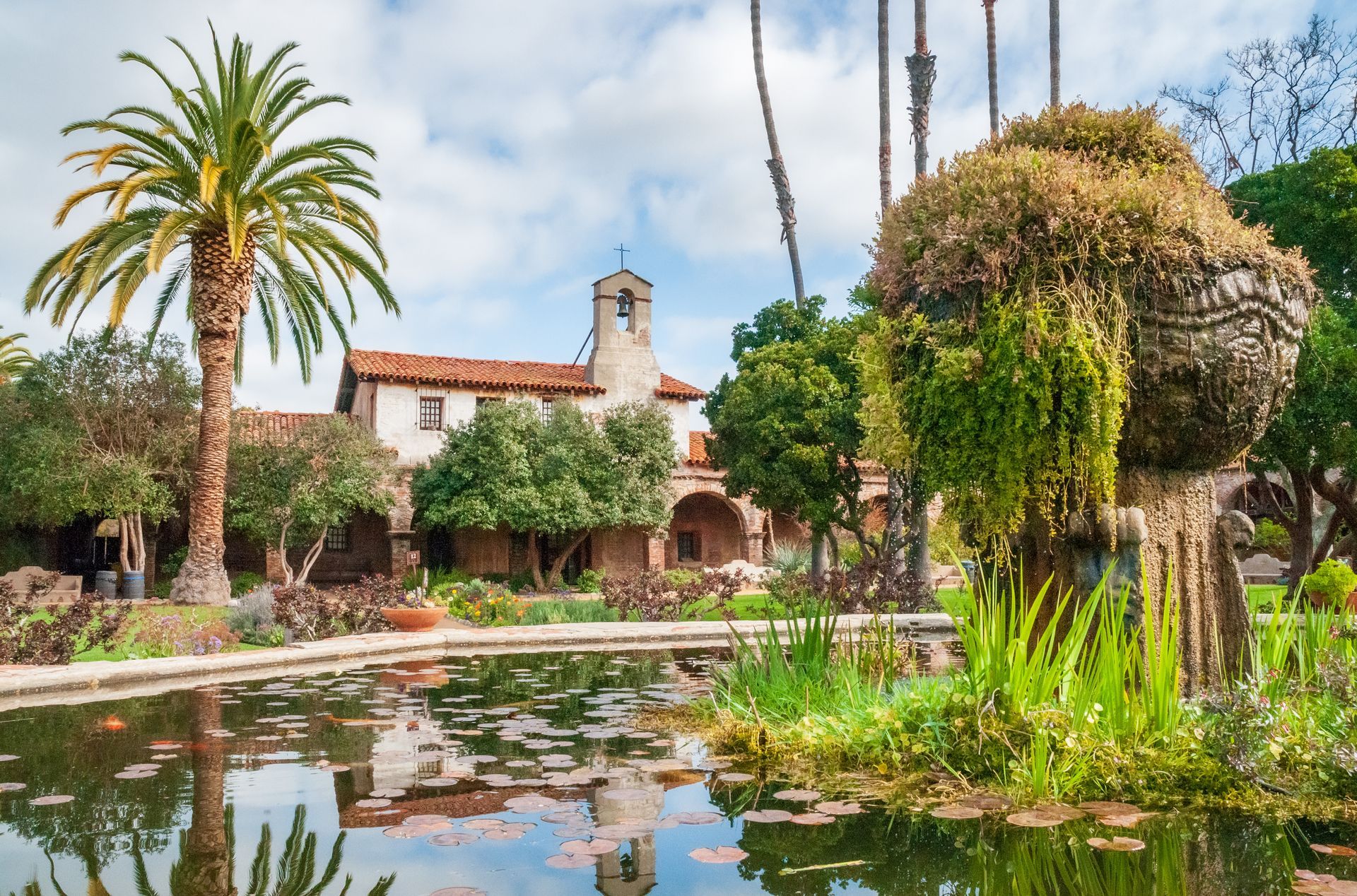 A pond with a statue in the middle of it and a building in the background.