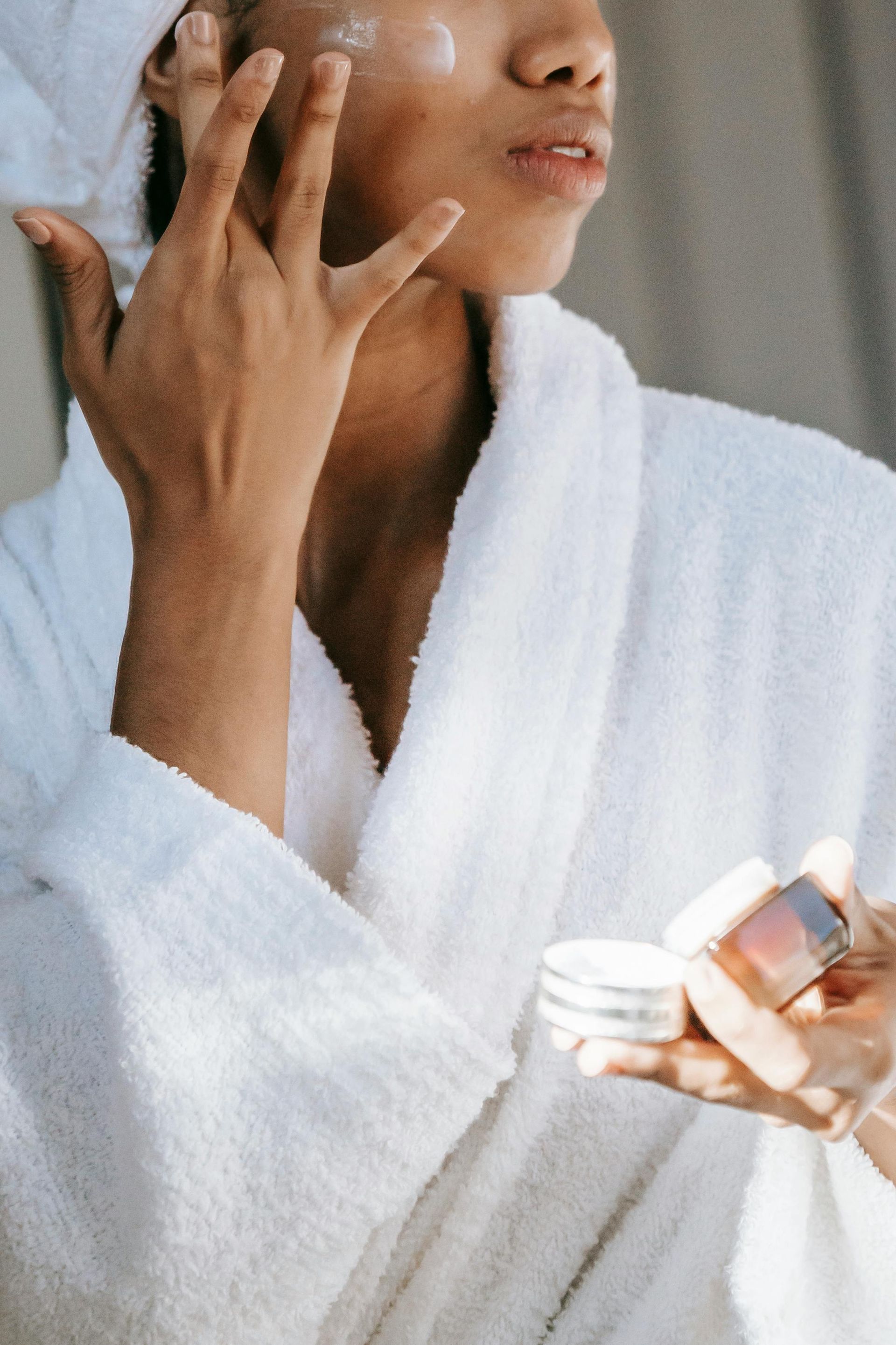 A woman in a spa robe applying skincare products for a rejuvenating routine at Devine Medspa.
