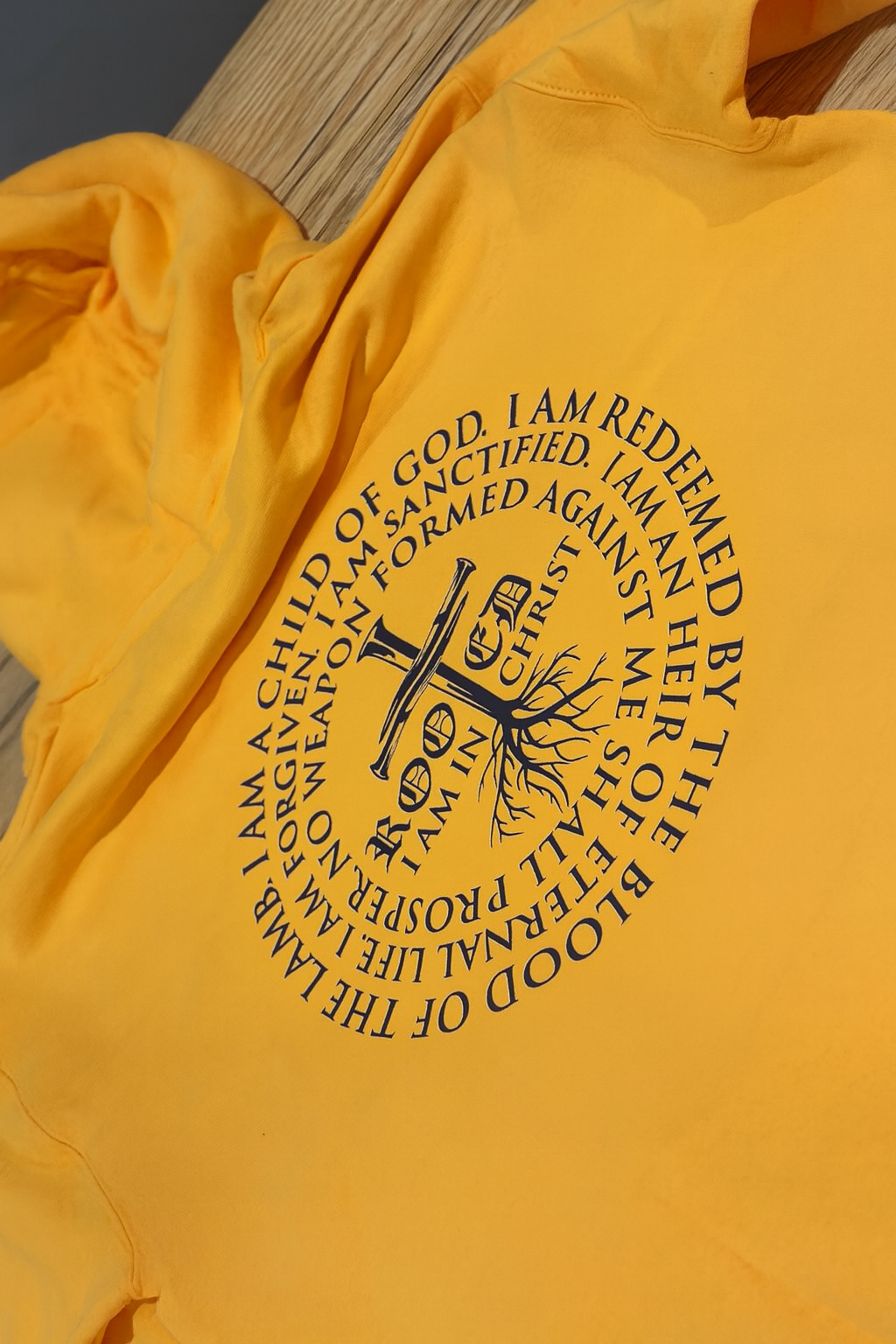 Yellow hoodie with a black circular design featuring a cross, tree, and text: "I am in Christ."