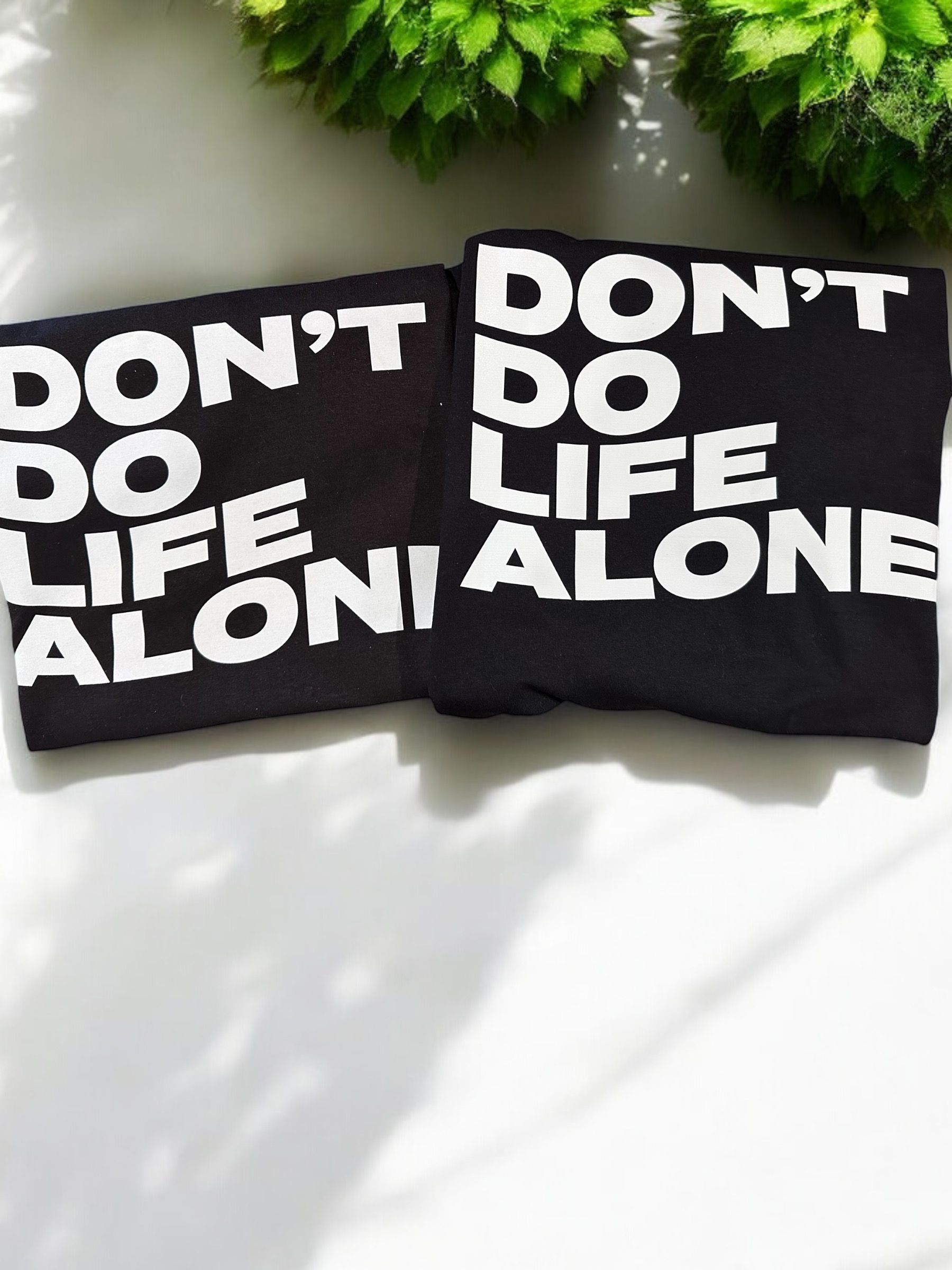 Two black t-shirts folded, stacked, with white text: "Don't do life alone."