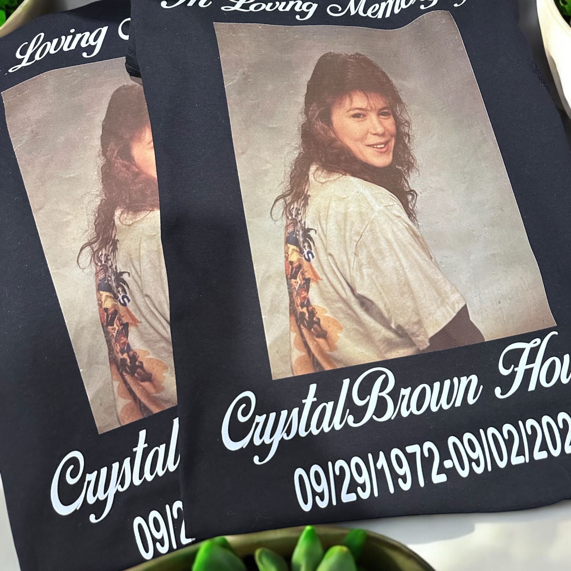 Two black memorial shirts with a photo of a woman, "Crystal Brown House," and dates.