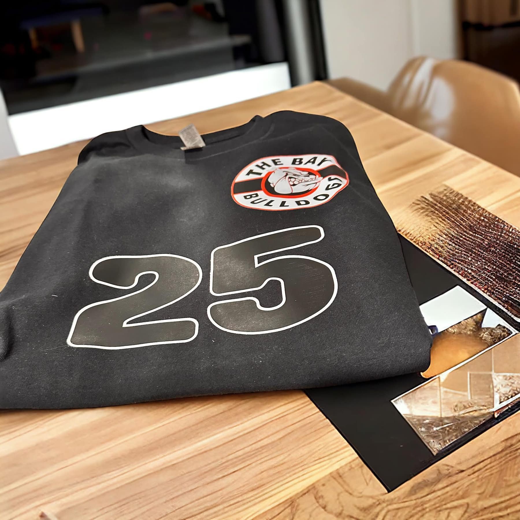 Black sweatshirt with "25" and a bulldog logo on a table with photos.