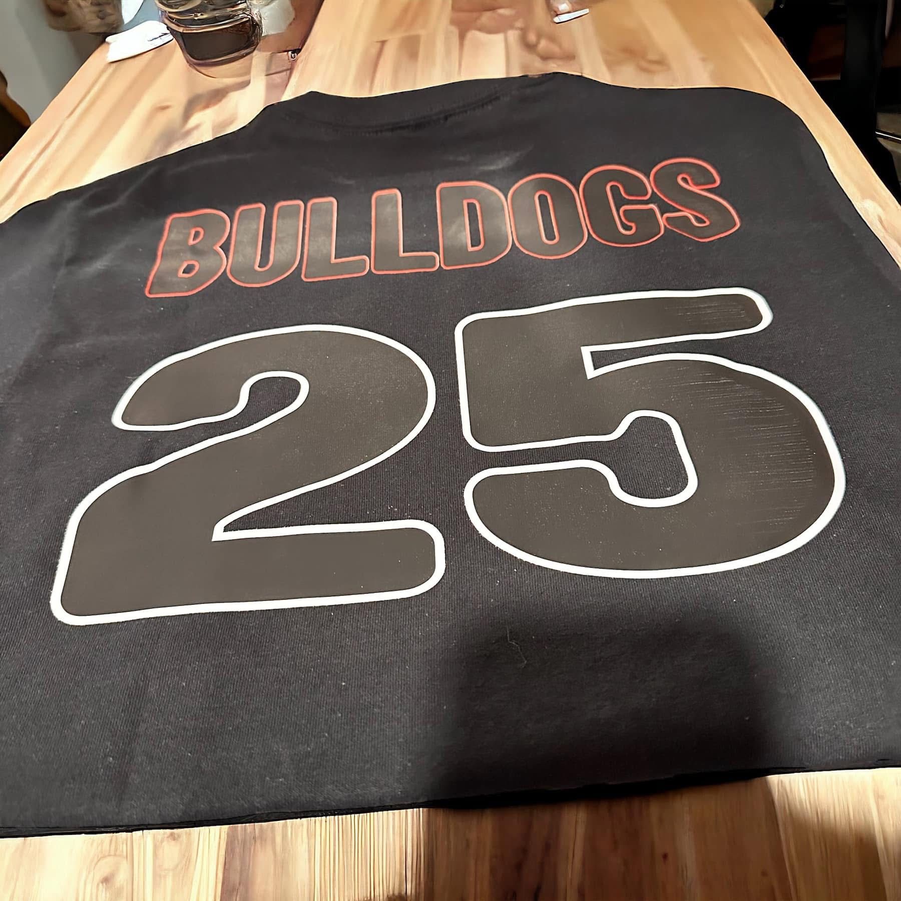 Black Bulldogs jersey with white-outlined black "25" and red-outlined "BULLDOGS" on a wooden table.