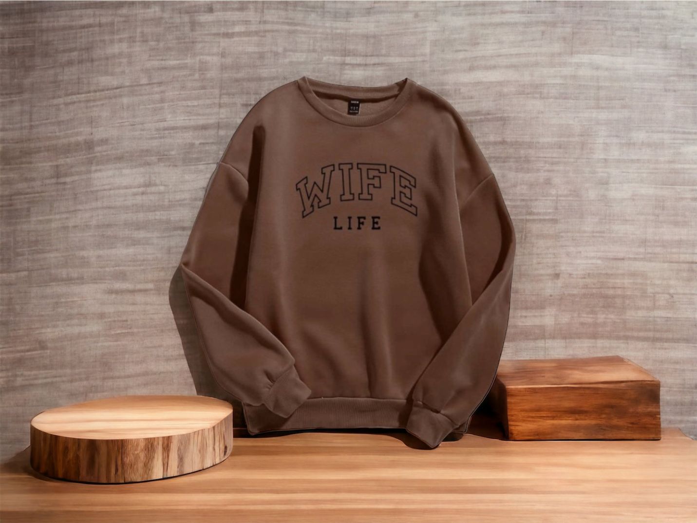 Brown sweatshirt with "WIFE LIFE" text, displayed on a wooden table.