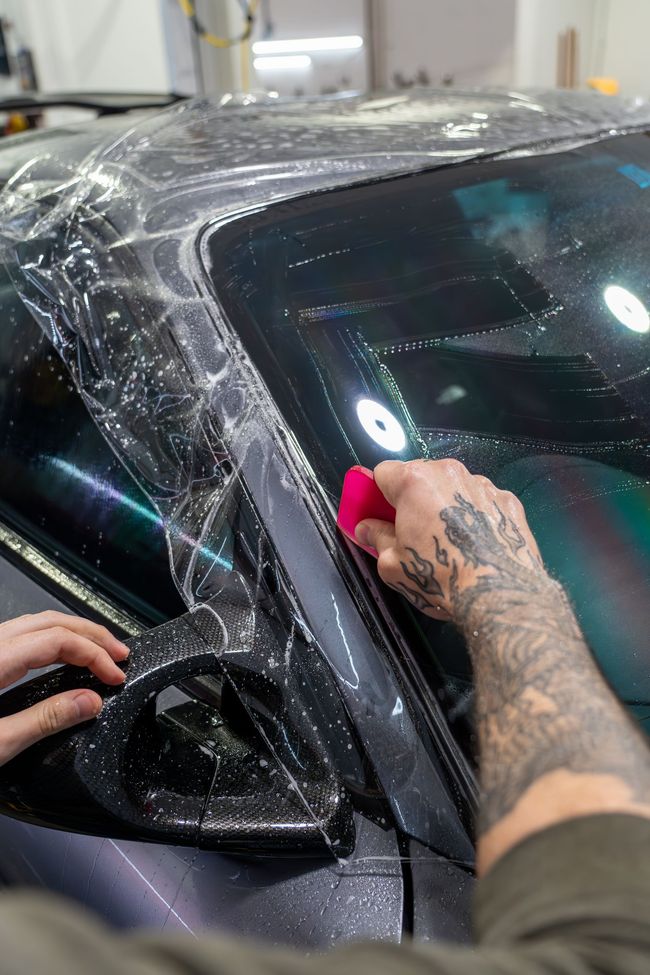 A man is applying a protective film to the windshield of a car.