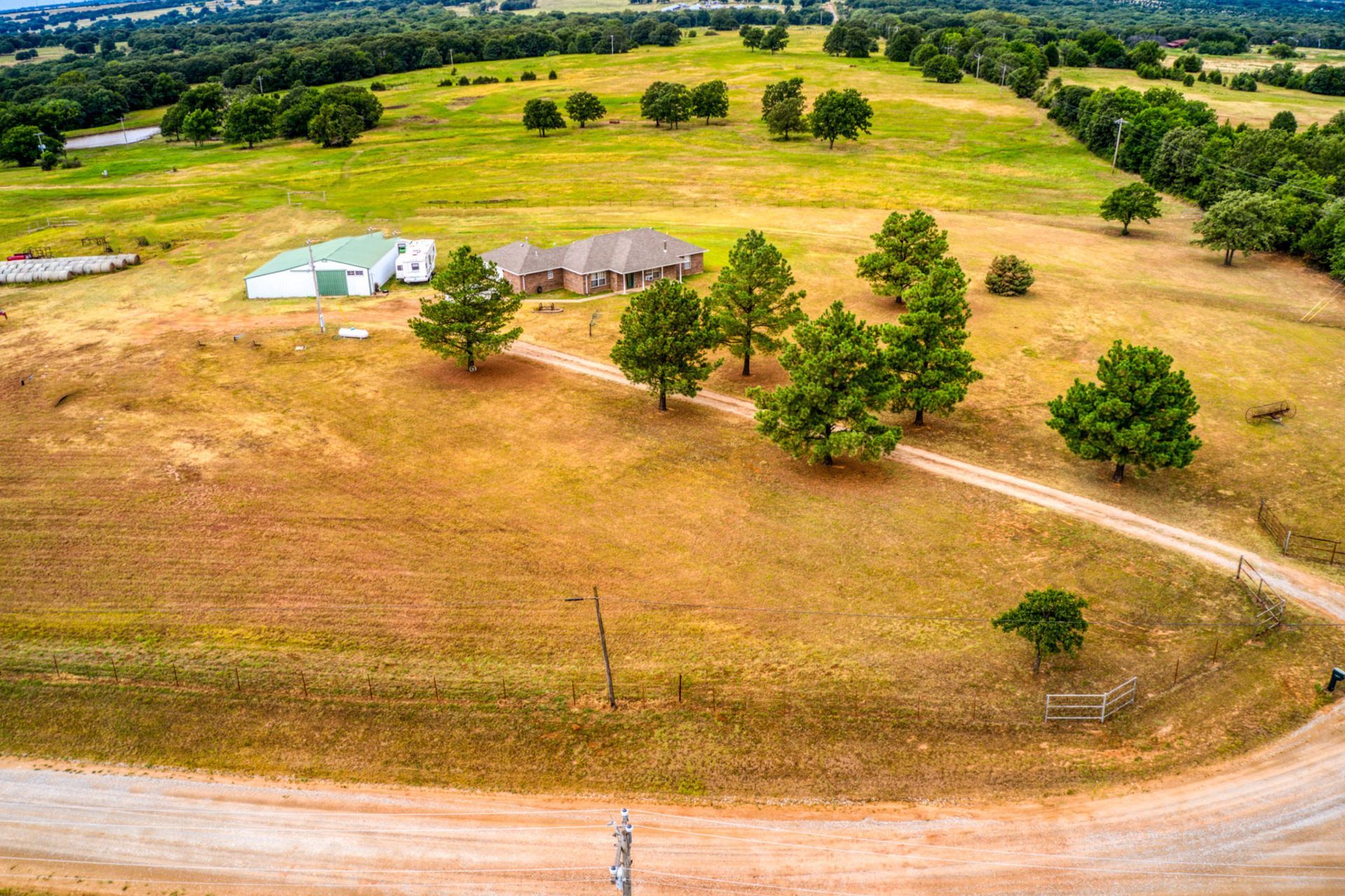 Aerial view of a home and barn on a grassy lot with a winding dirt road and trees.