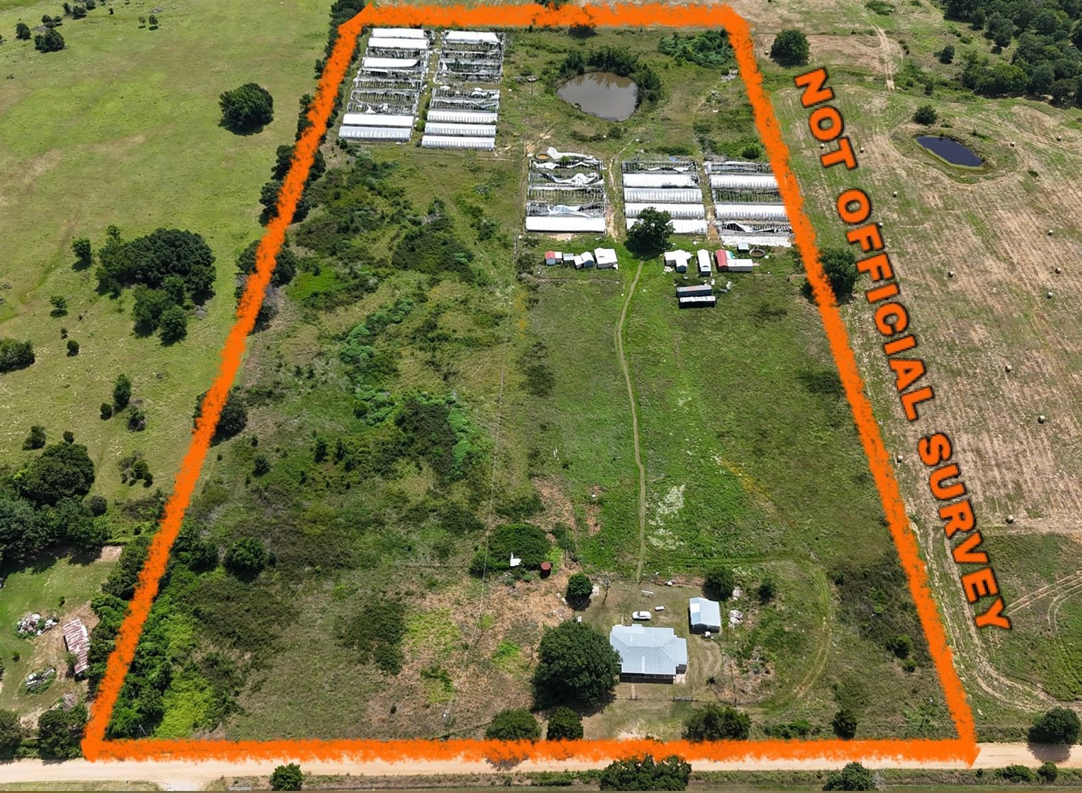 Aerial view of a rural property with buildings, a pond, and a large open field outlined in orange.