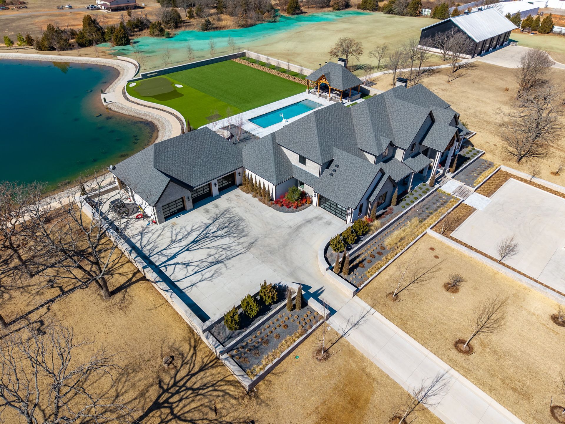 House on a grassy hill with a long driveway and trees.