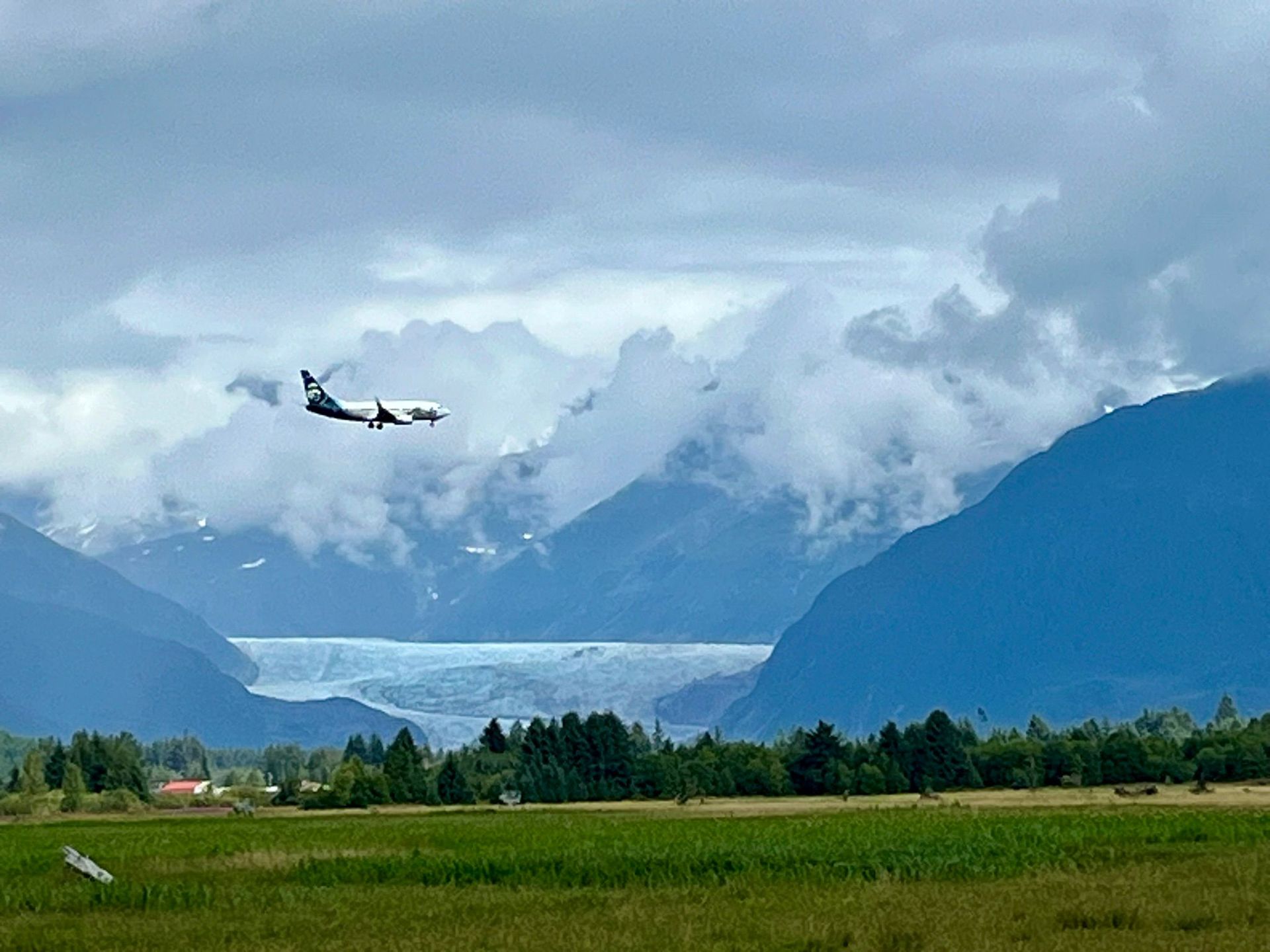 A plane is flying over a field with mountains in the background min Juneau AK. Local Tour Guide in Juneau, AK. 