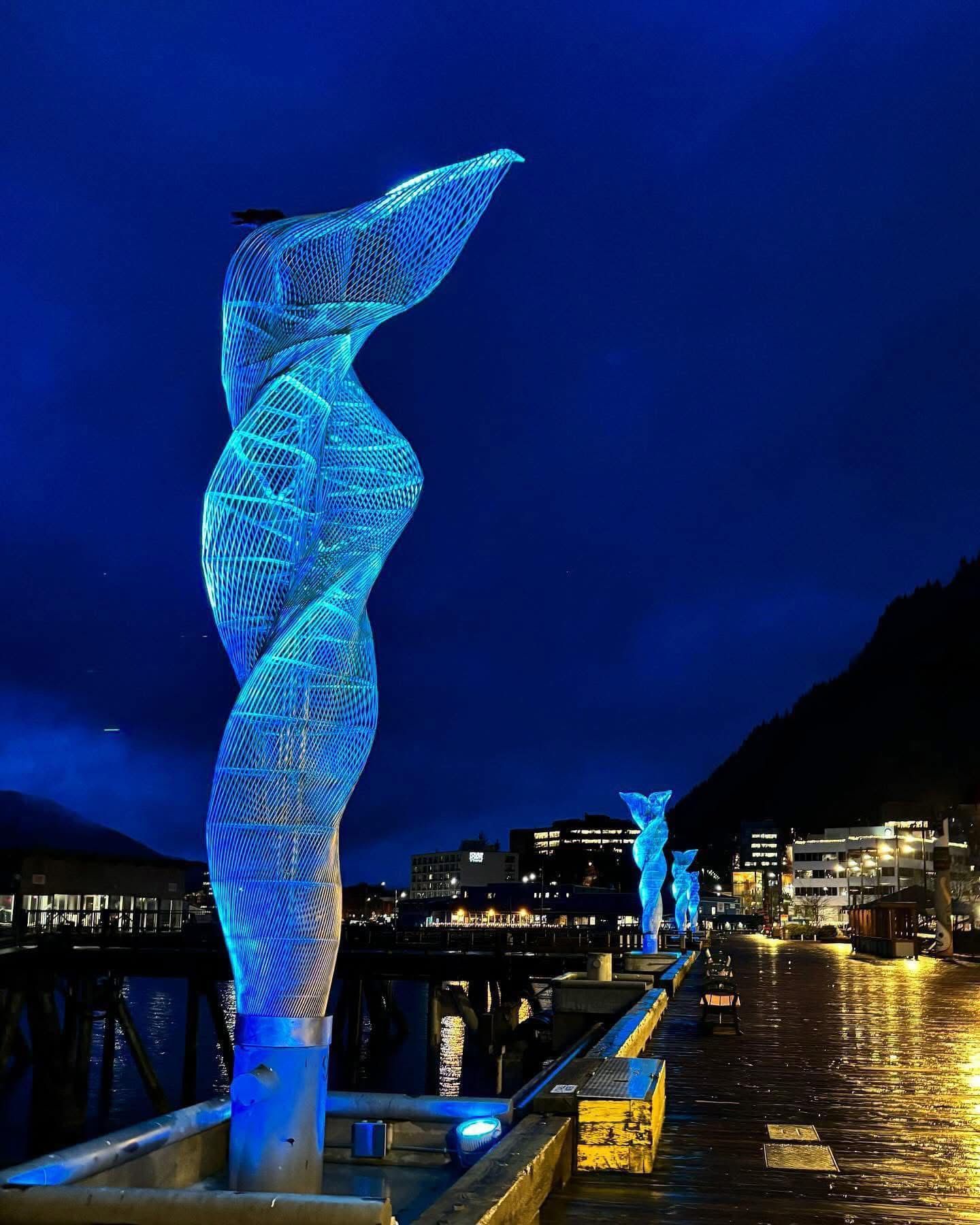 A sculpture is lit up with blue lights at night in Juneau AK. Local Tour Guide