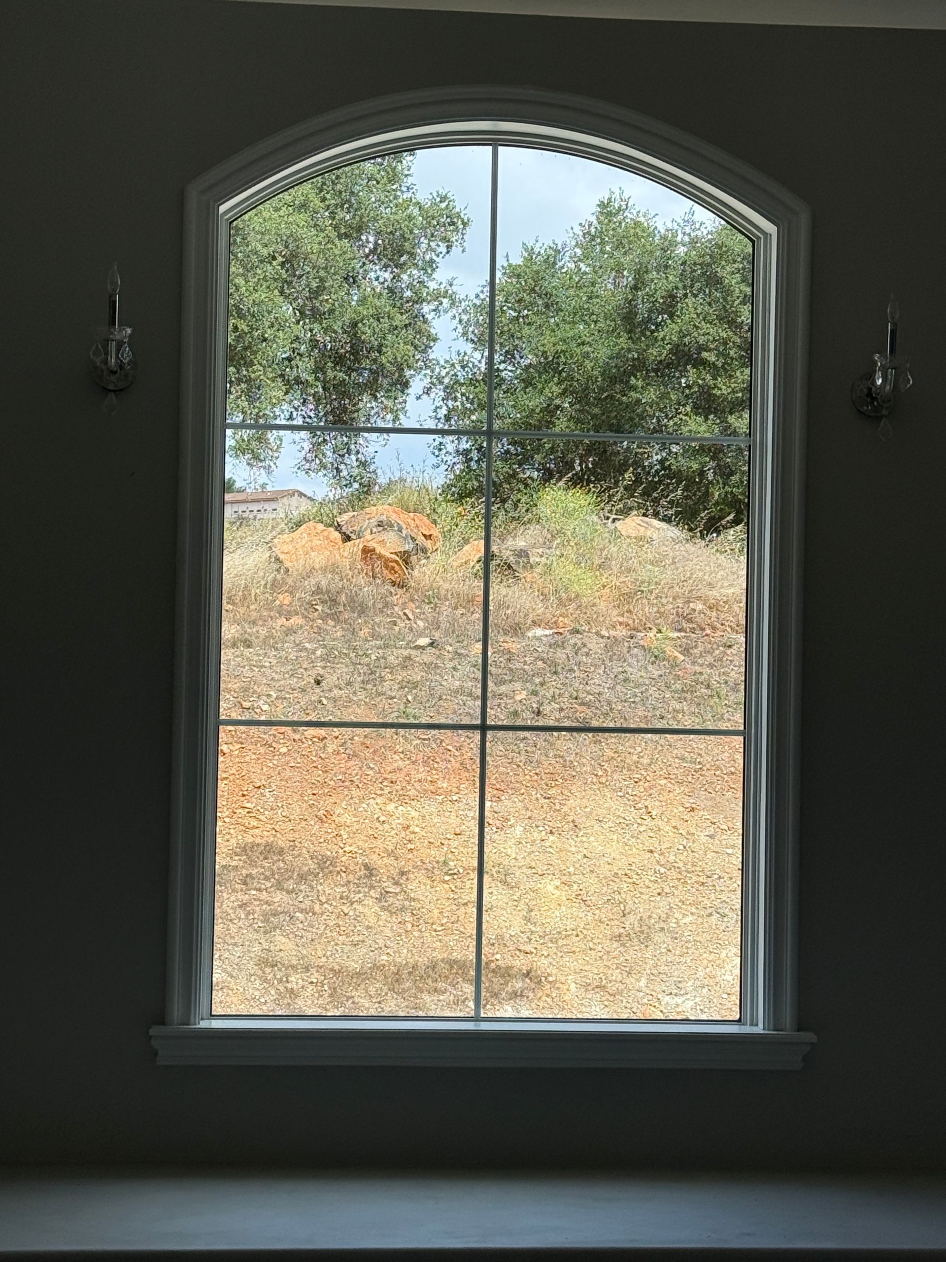 Arched window overlooking a dry hillside with trees and blue sky