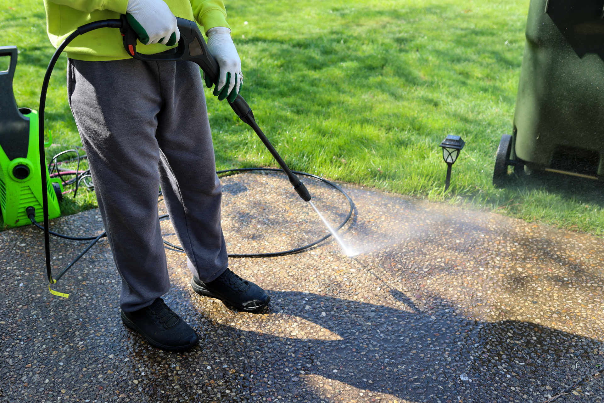 Person pressure-washing a gravel driveway with a green machine, spraying water across the surface