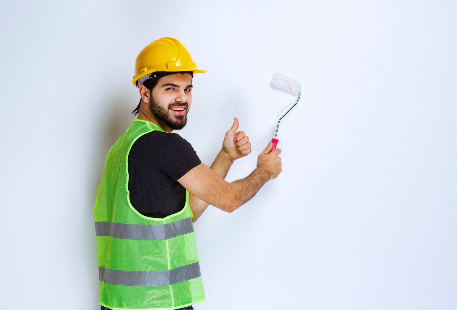 A man in a hard hat is holding a paint roller and giving a thumbs up.