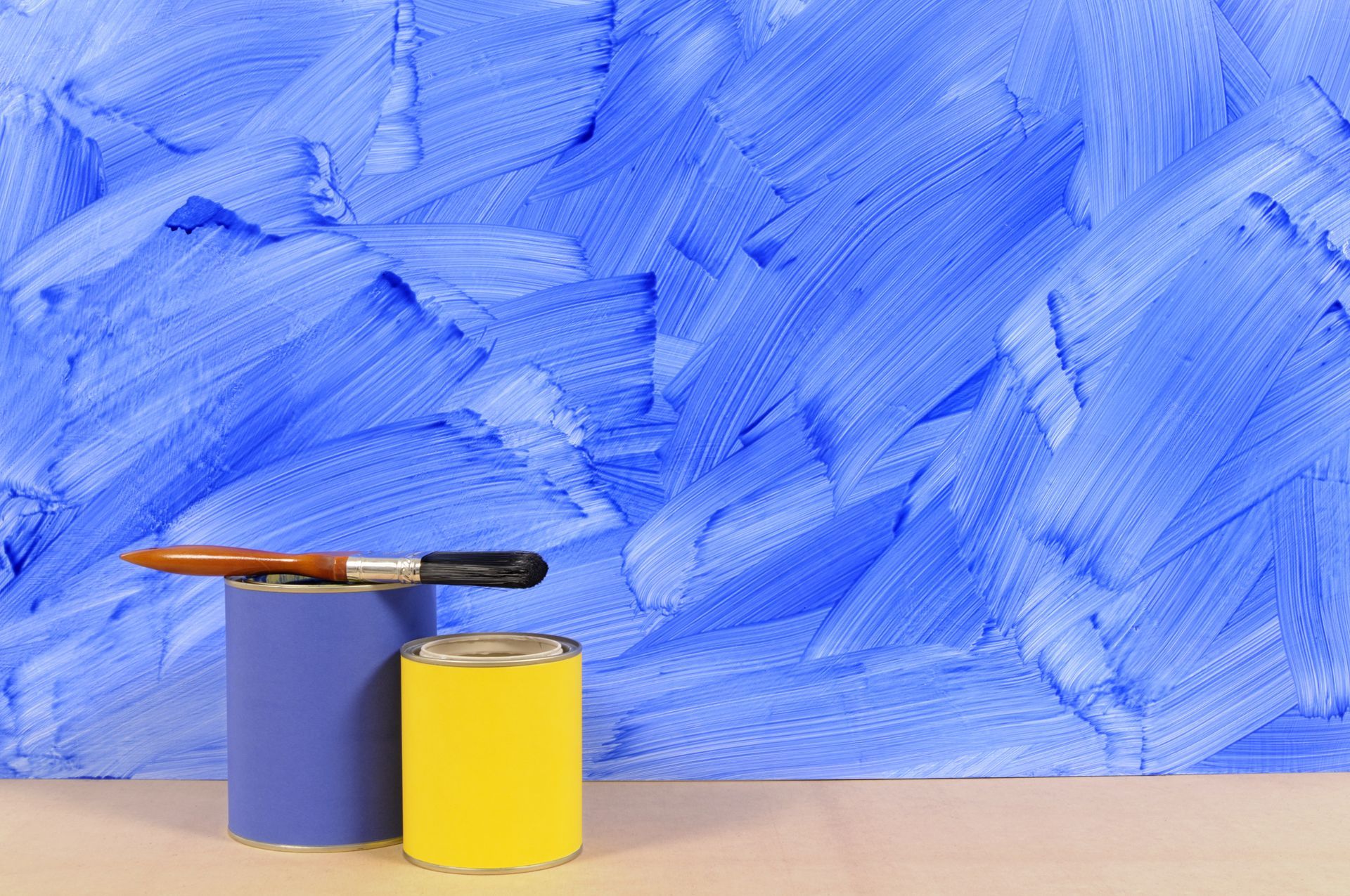 Two cans of paint and a brush are on a table in front of a blue wall.