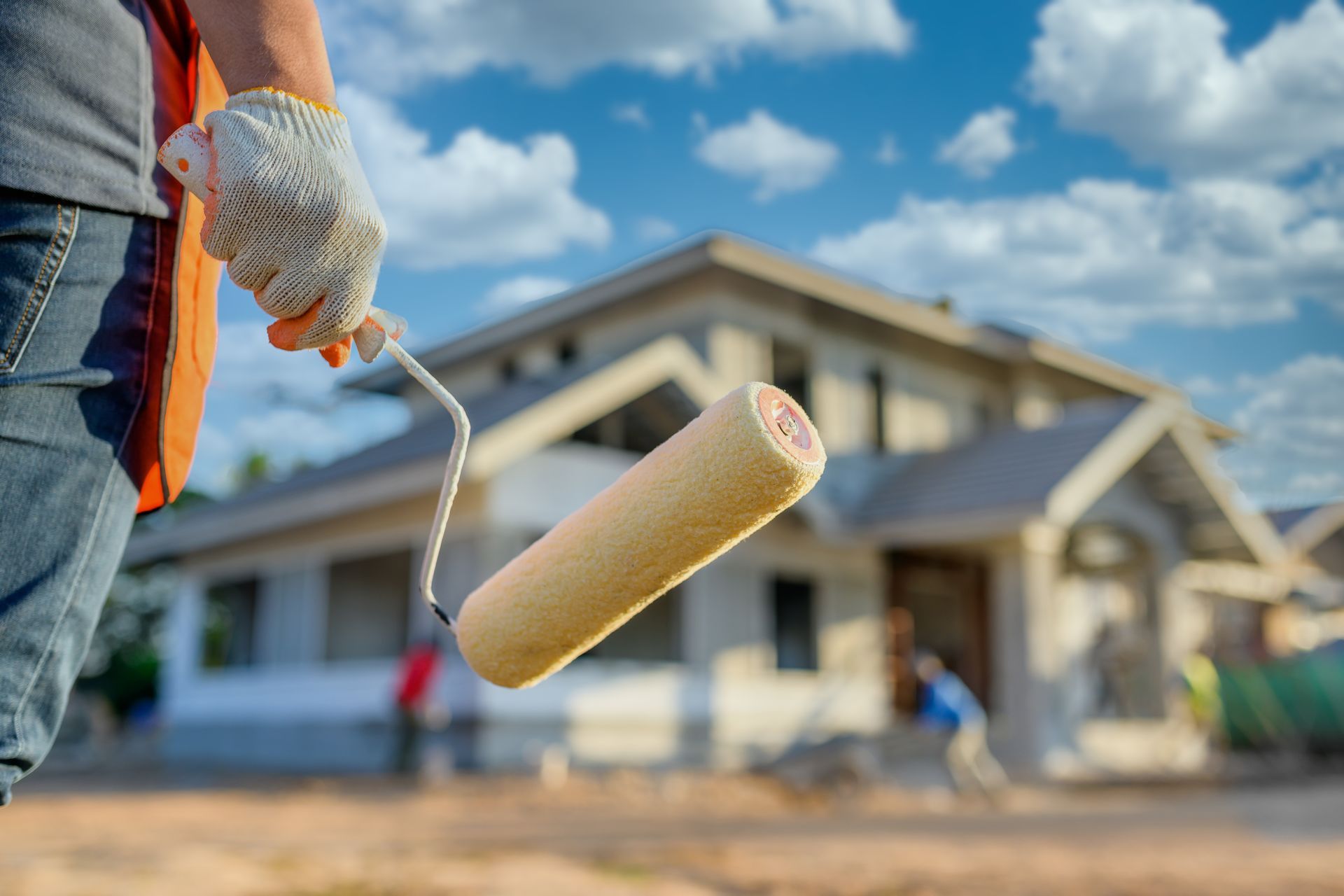 A man is holding a paint roller in front of a house under construction.