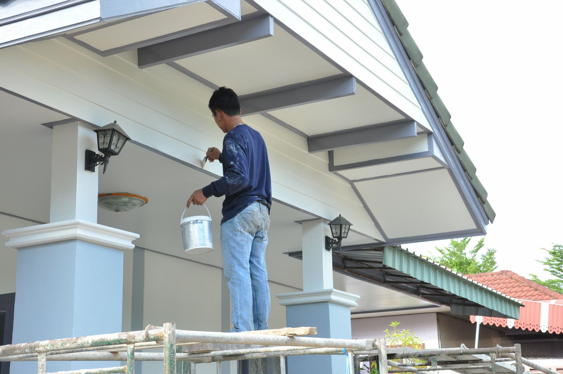 A man is painting a house with a bucket of paint.