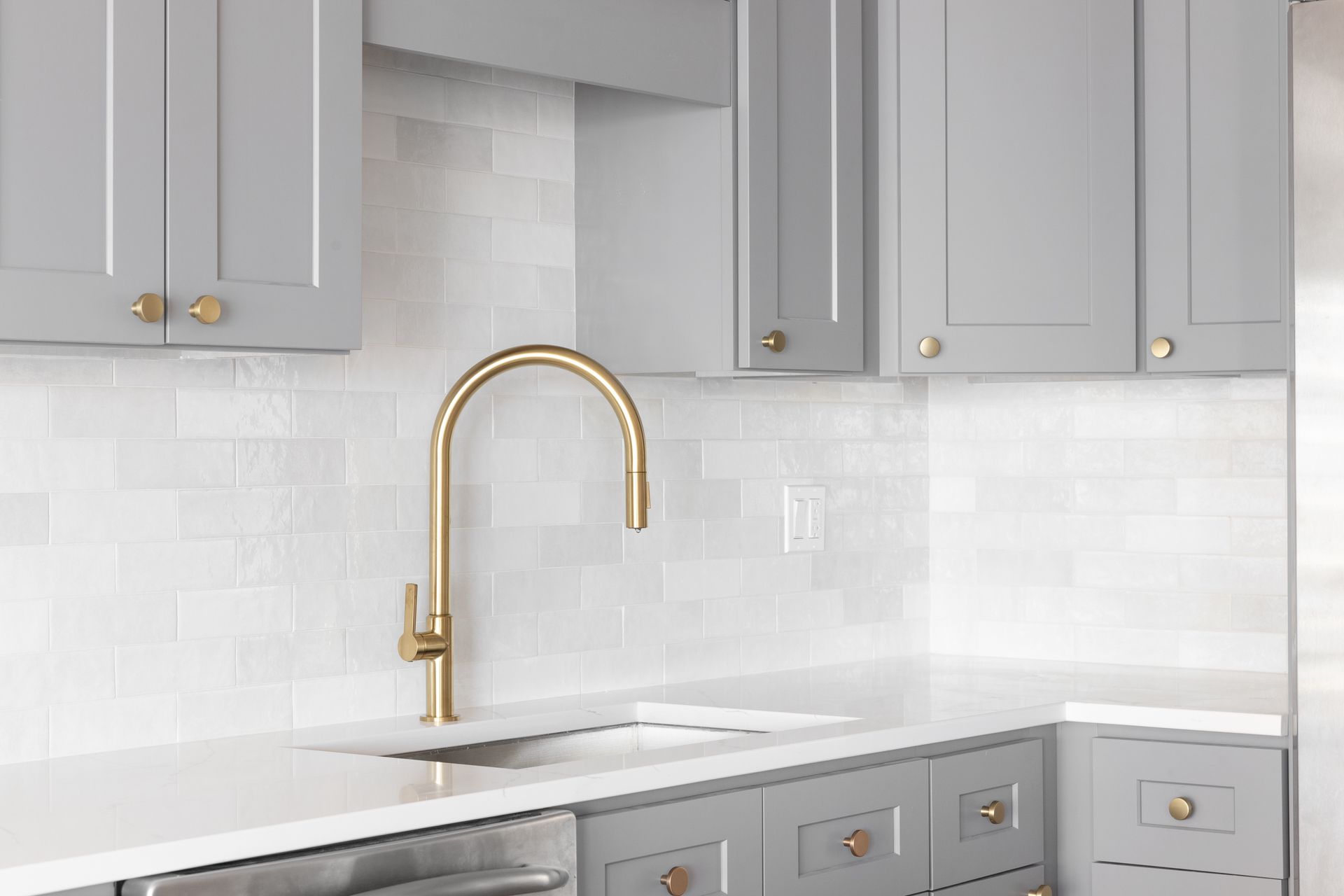 A kitchen with gray cabinets and a gold faucet.