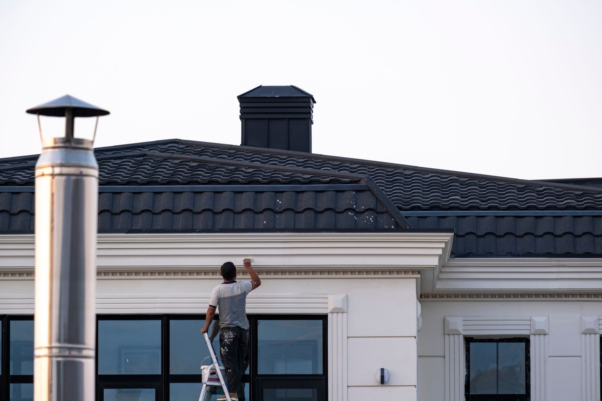 A man on a ladder is painting the roof of a house.