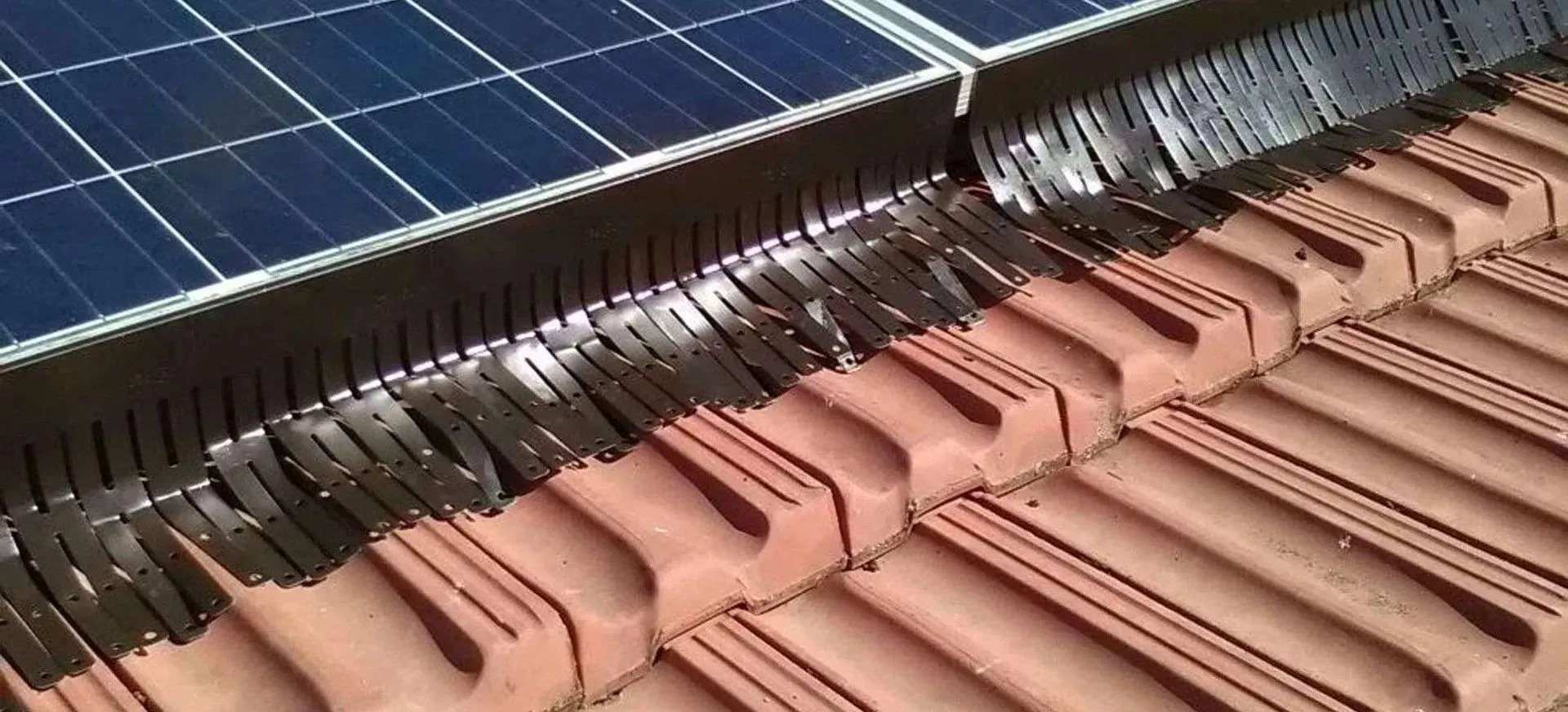 Pannelli solari accanto a un tetto di tegole con grondaie protette da griglie che raccolgono foglie e detriti.