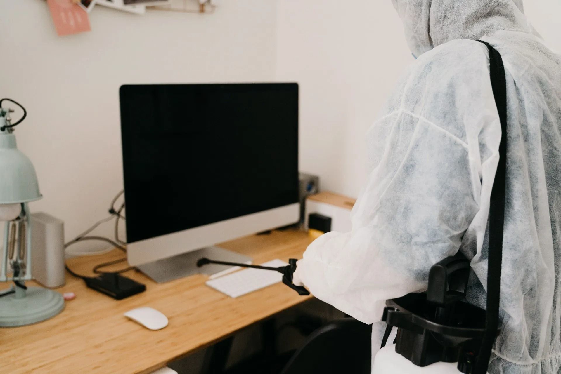 Persona con indumenti protettivi seduta a una scrivania con monitor e lampada.