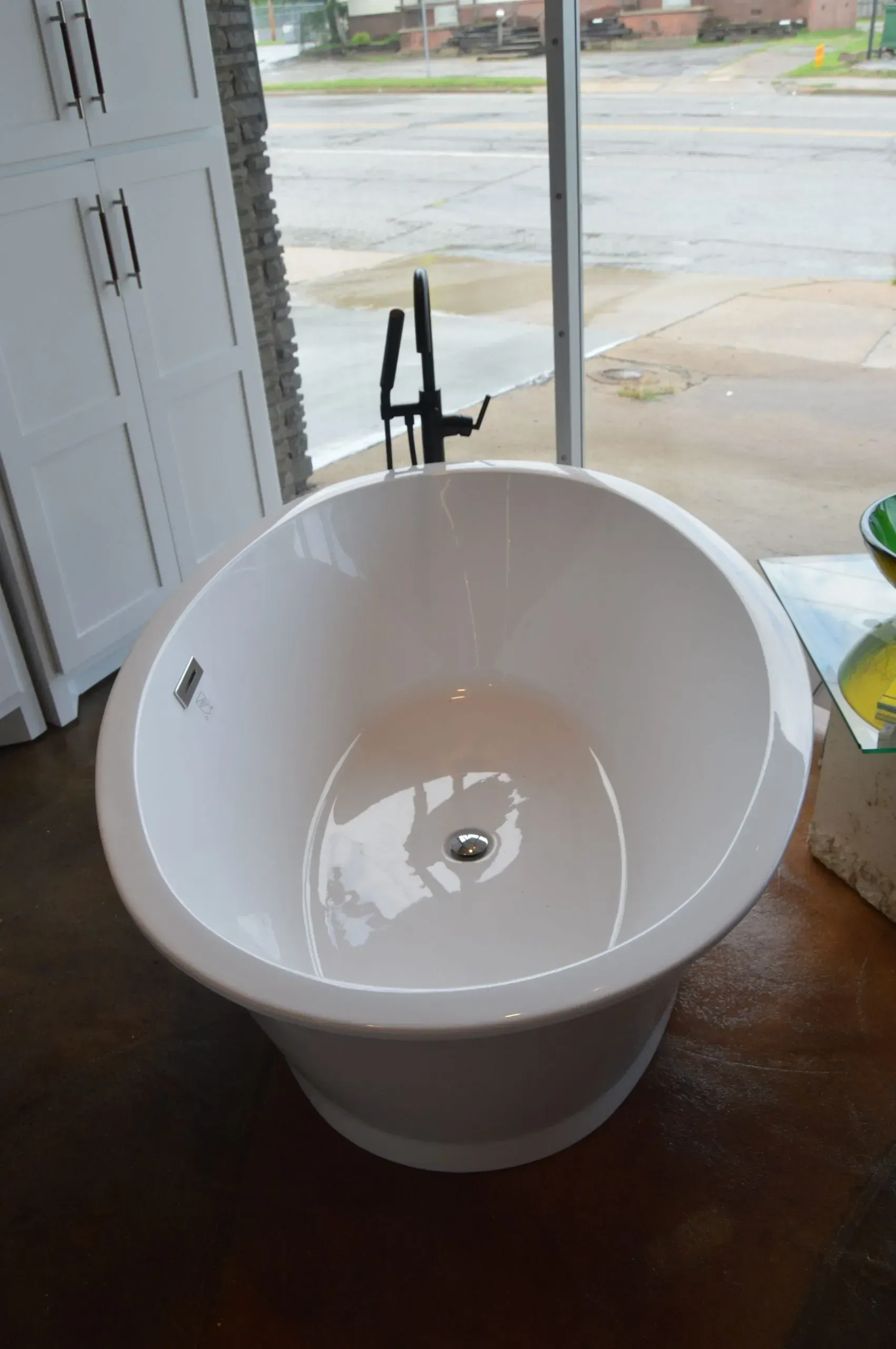 A white bathtub is sitting on a wooden floor in front of a window.