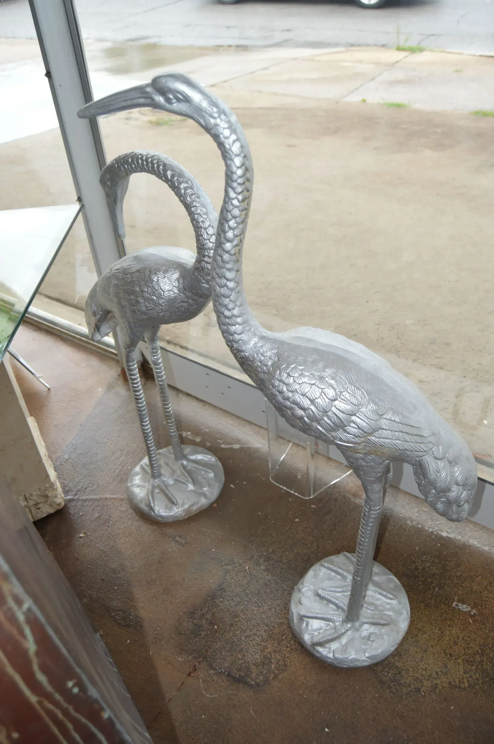 Two silver birds are standing next to each other in front of a window