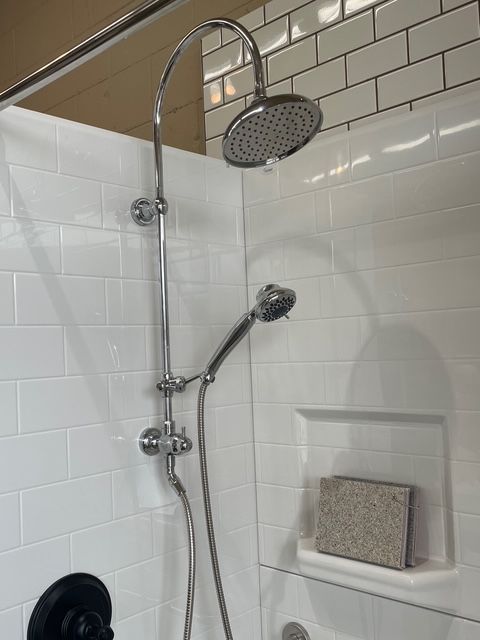 There is a shower head in the shower with white tiles.