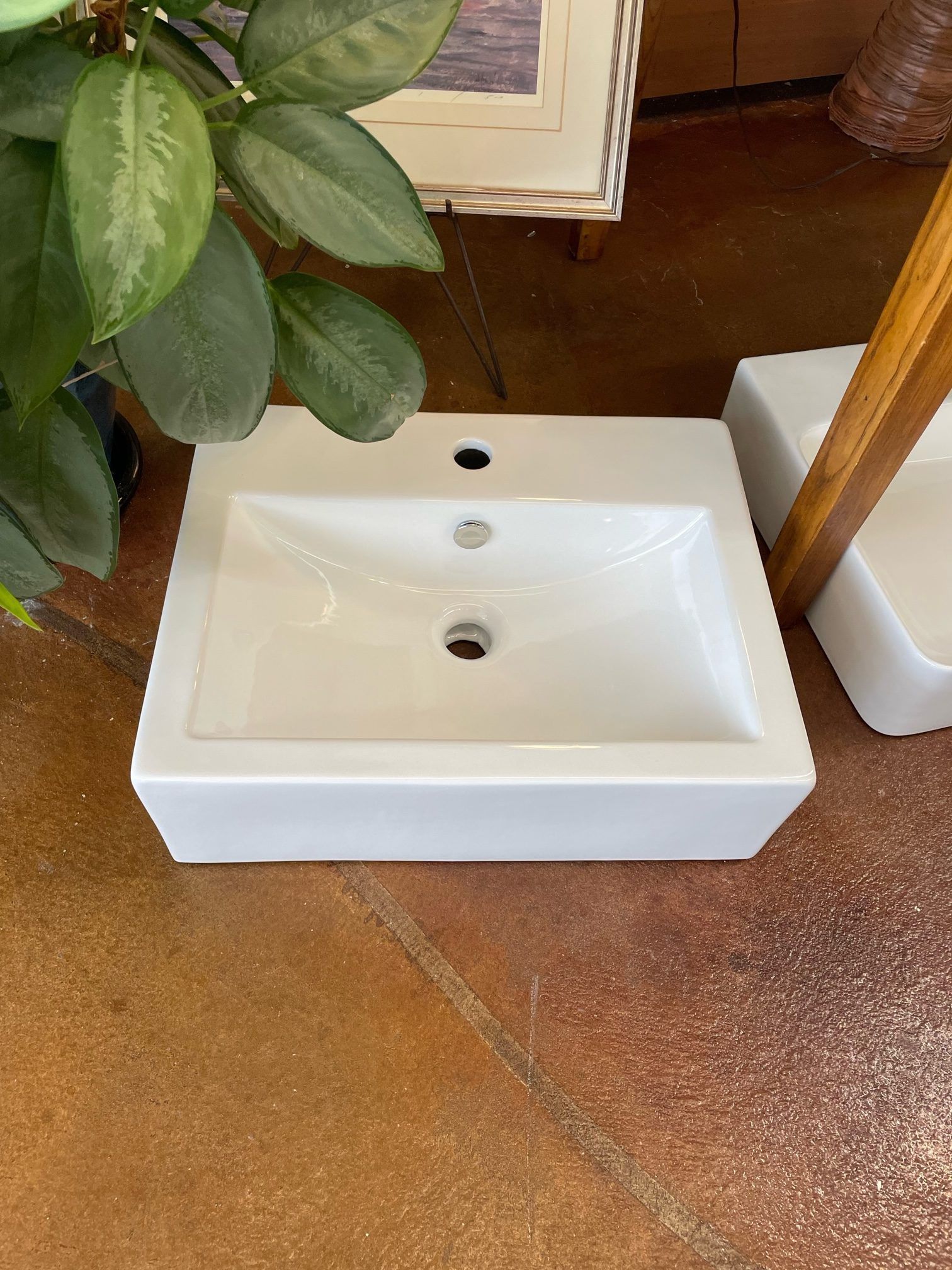 A white sink is sitting on a tiled floor next to a plant.