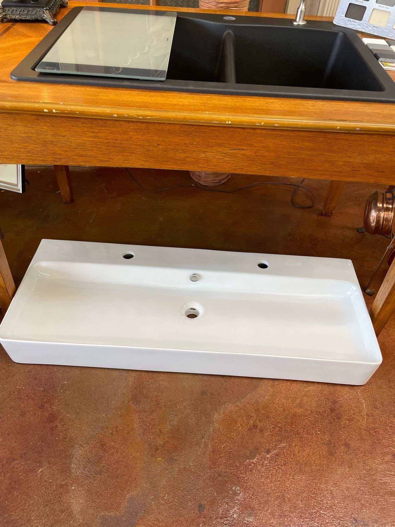 A white sink is sitting under a black sink on a wooden table.