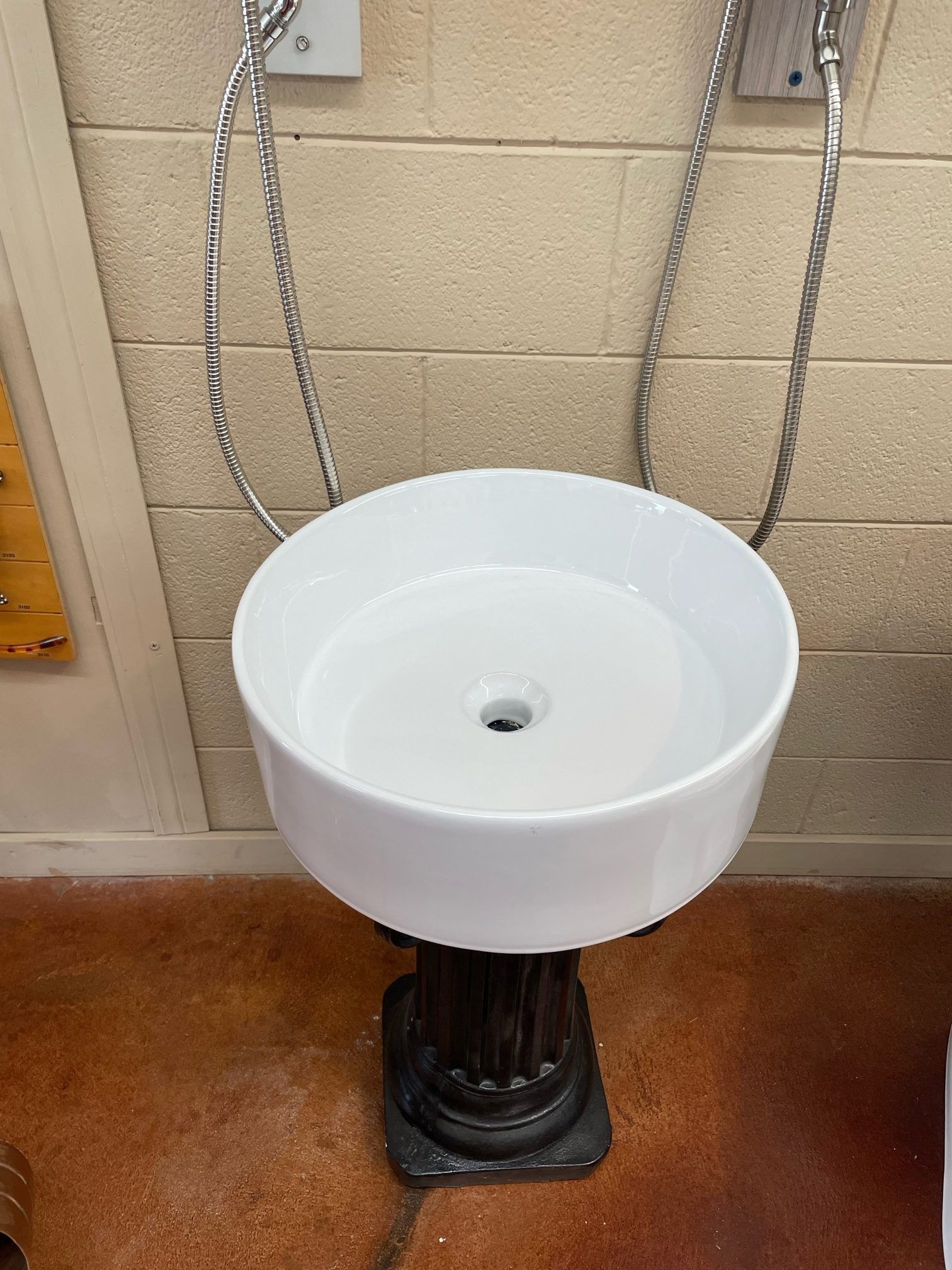 A white sink is sitting on a pedestal in front of a brick wall.