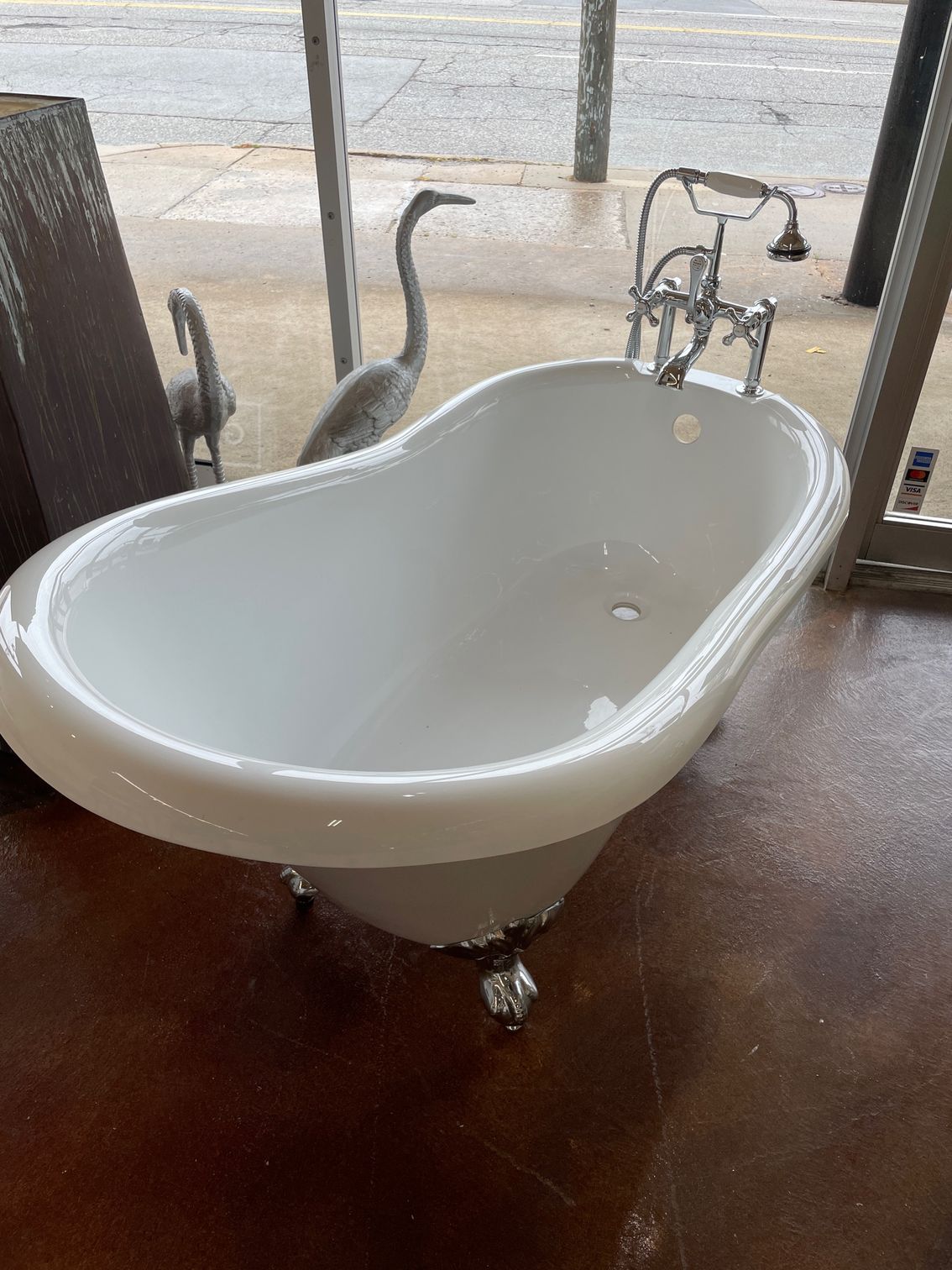 A white bathtub is sitting on a wooden floor next to a window.
