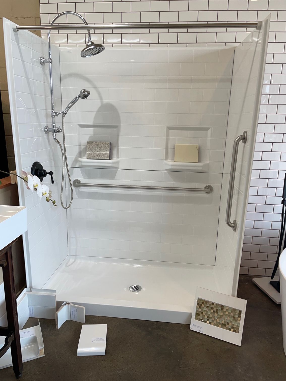 A white shower stall with a shower head and handles in a bathroom.