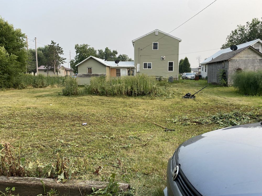 A car is parked in the grass in front of a house.