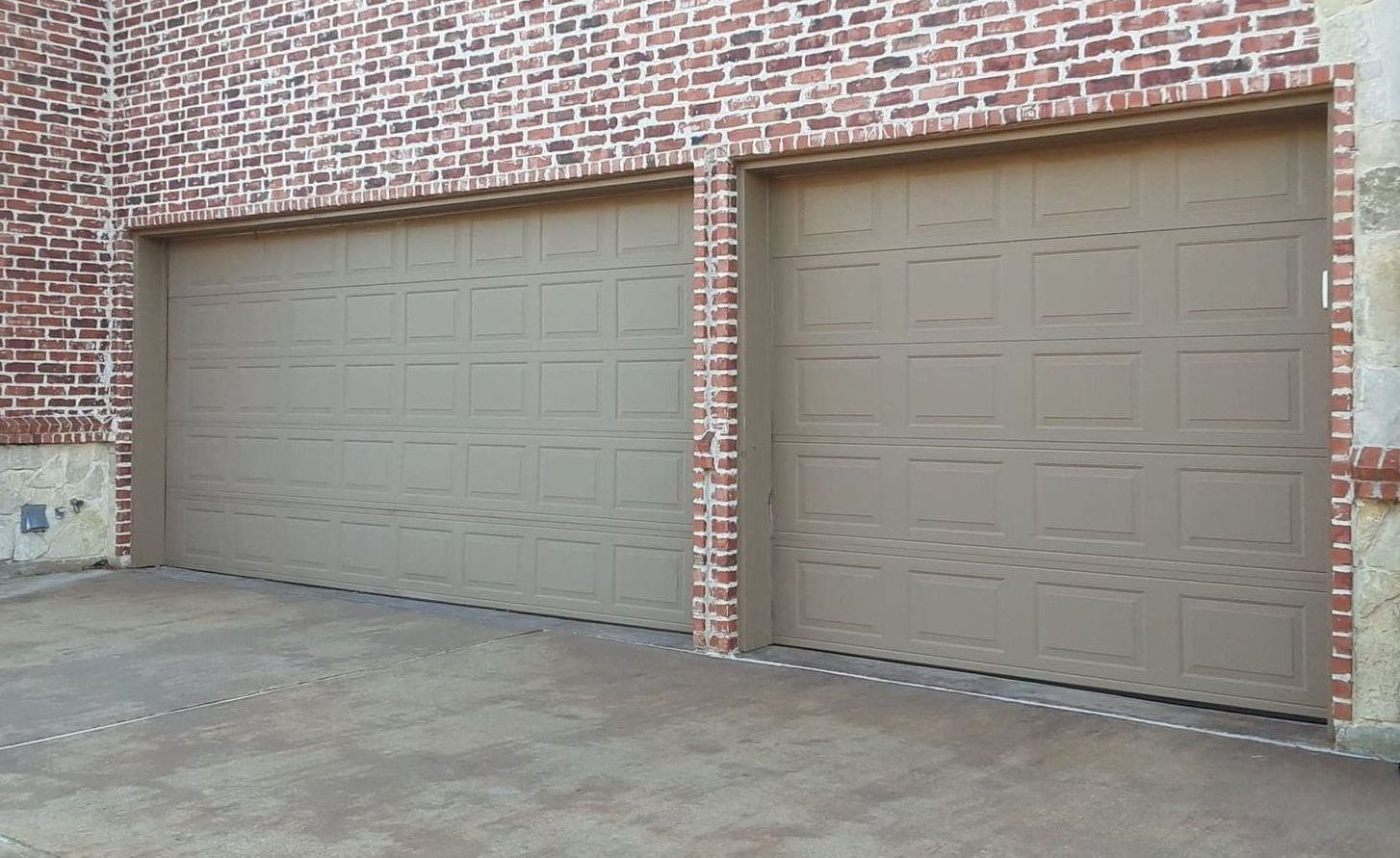 Two beige garage doors on a brick building with a concrete driveway.